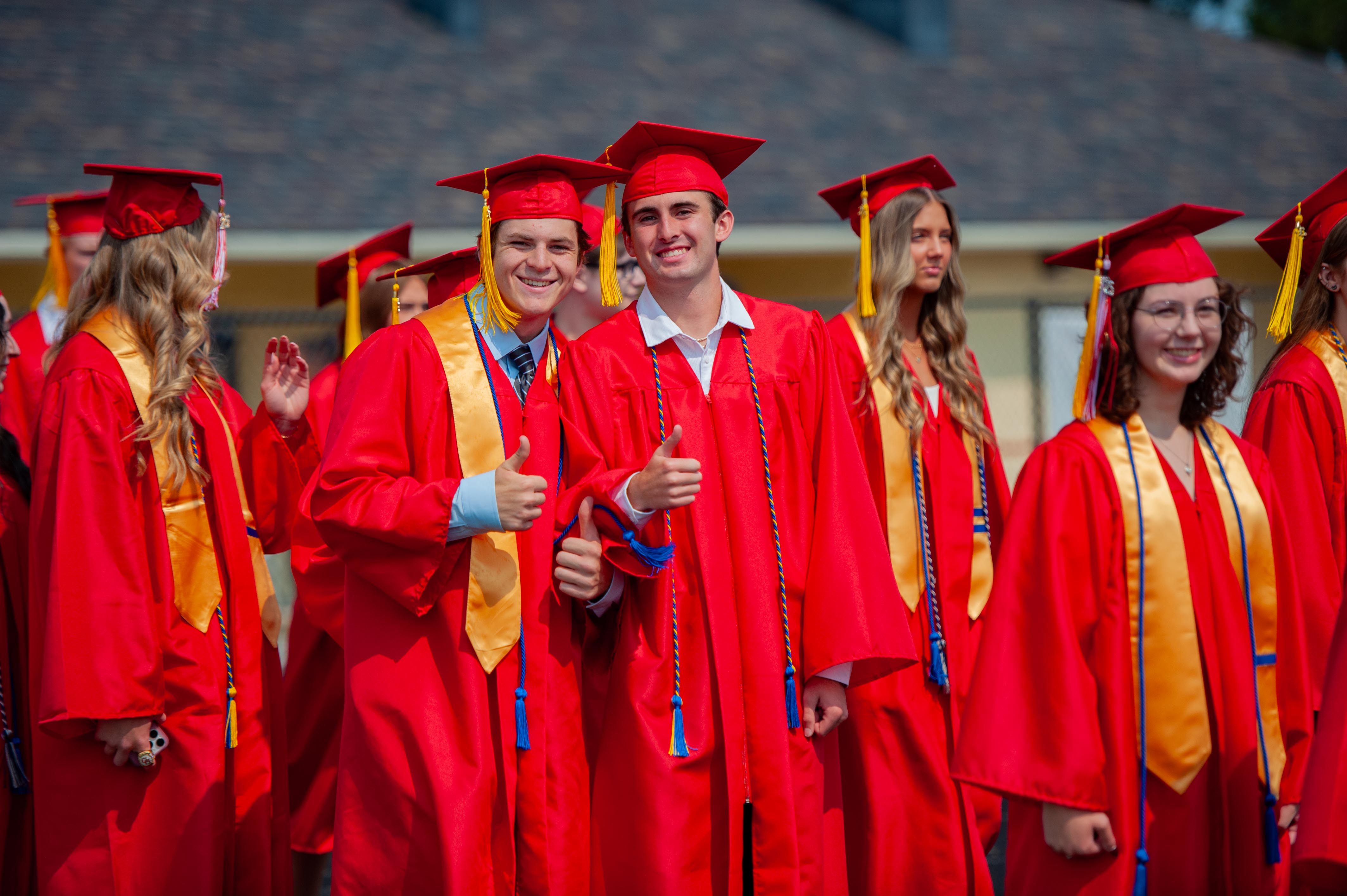 Graduates in red gowns and caps pose for photos in front of a building.