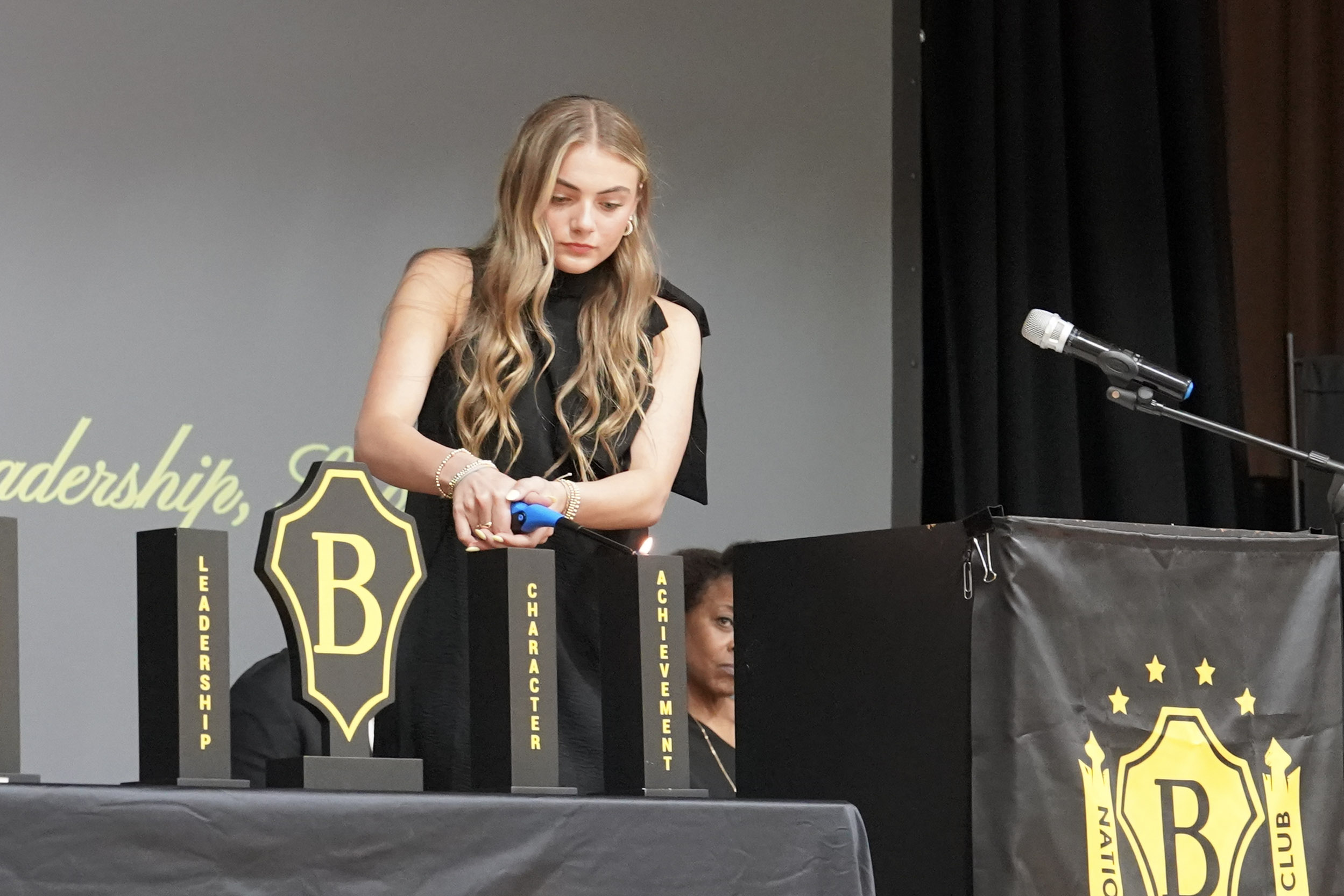 Girl on stage lights candle on table with Beta Club emblem