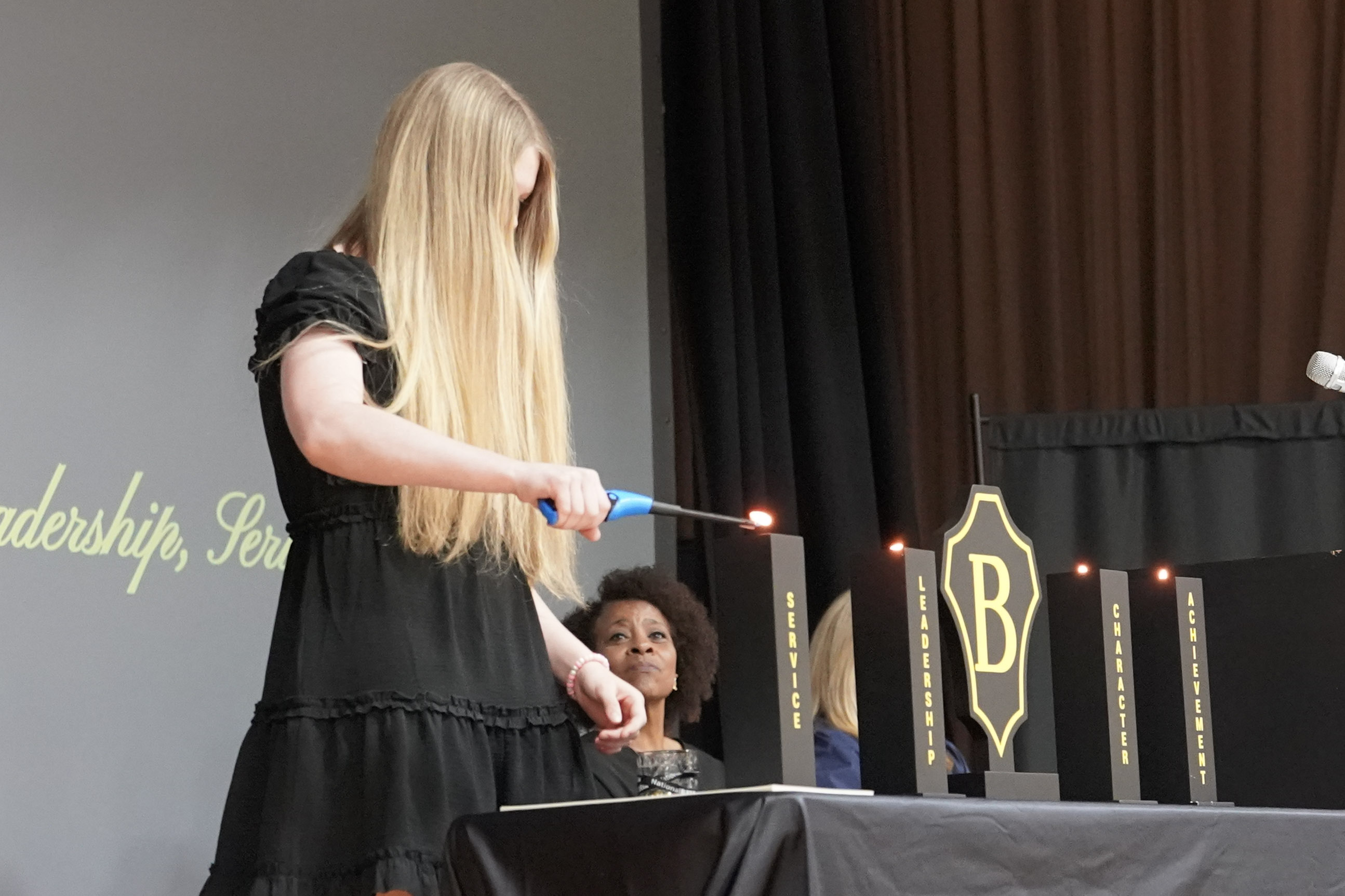Girl on stage lights candle on table with Beta Club emblem