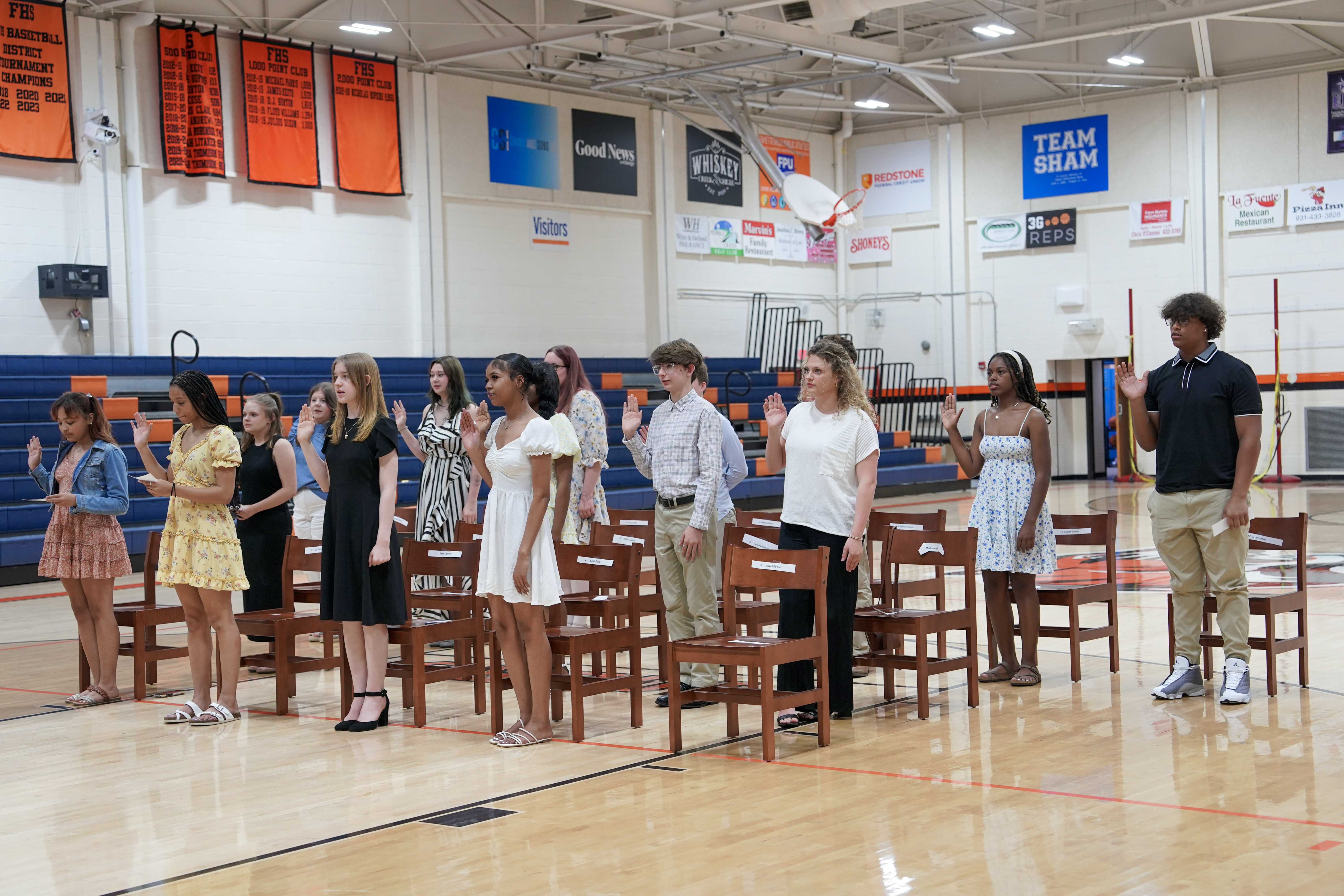 Students in a group on the gym floor raise right hands to take oath with banners in background