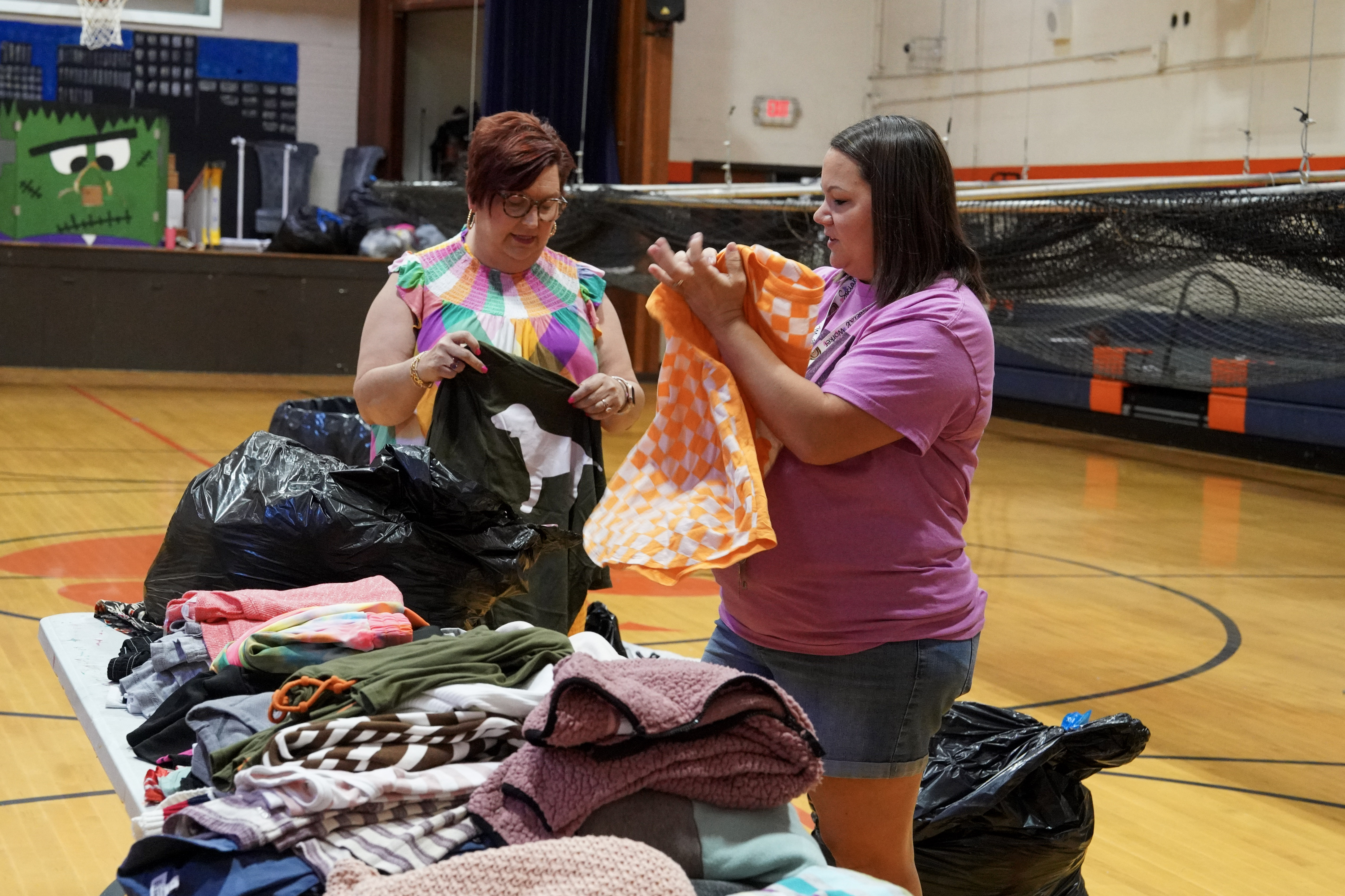 Two women folding clothes on table in gym floor