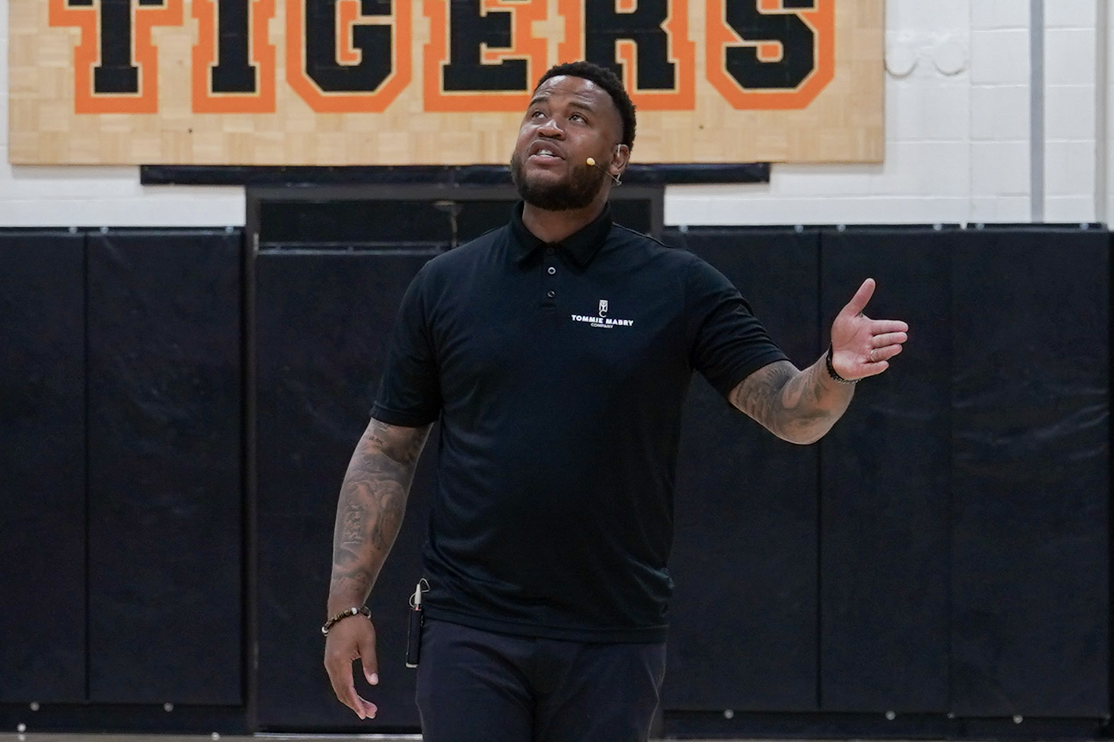 Man in black shirt and pants speaks with Tigers sign in background