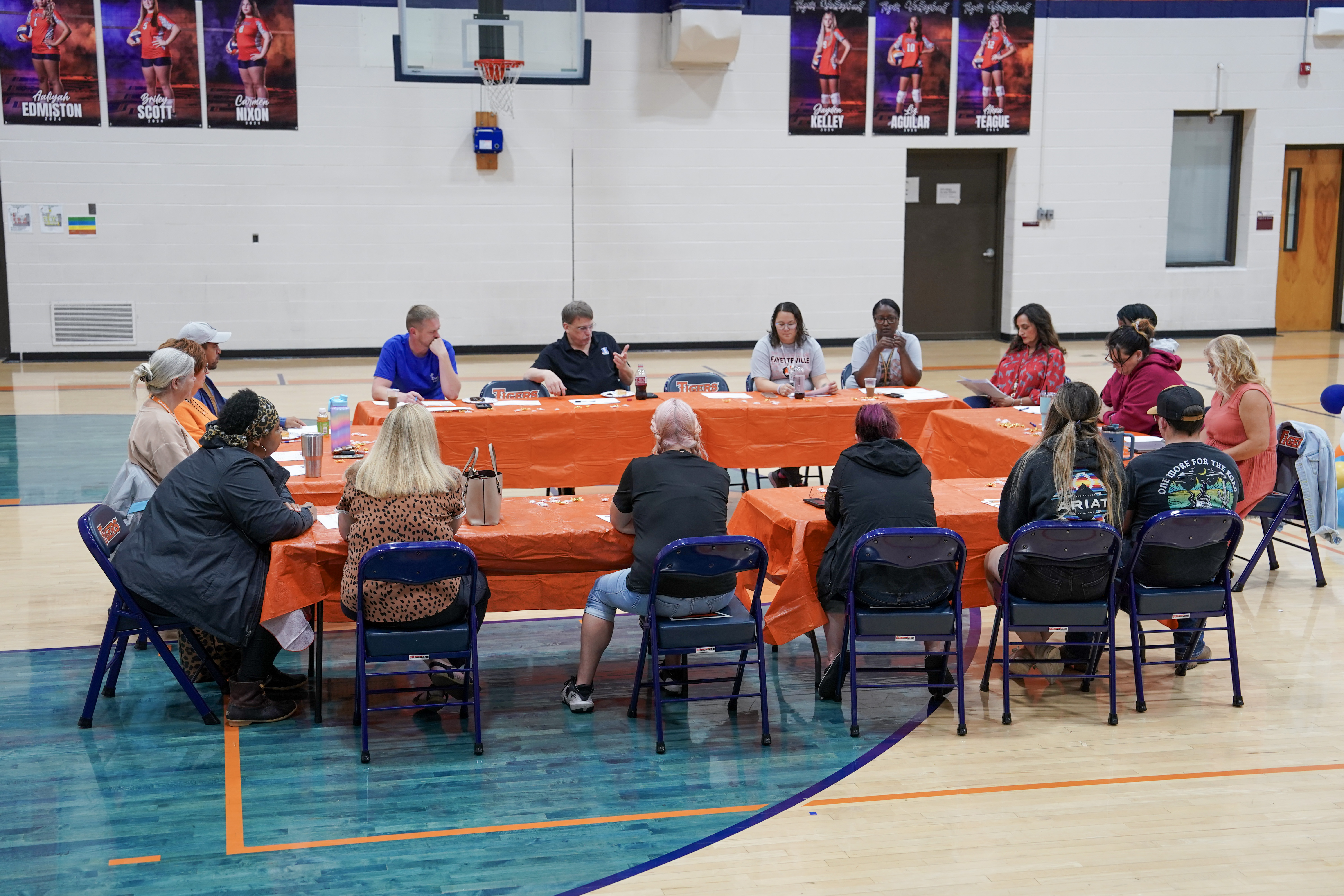 Several adults seated around a table with orange tablecloth in gymnasium