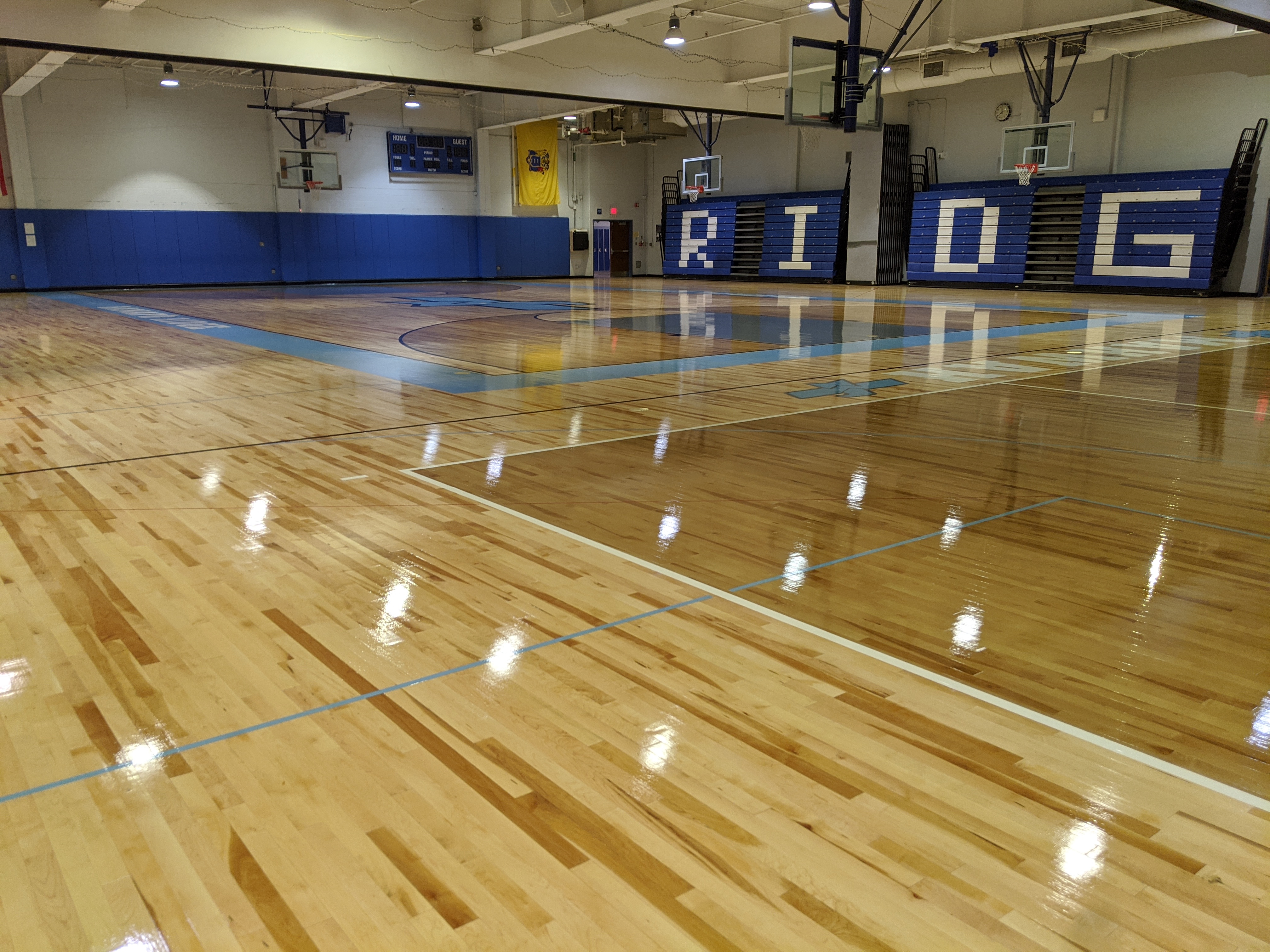 A polished wooden basketball court with blue wall padding and large "RIDG" letters on the back wall.