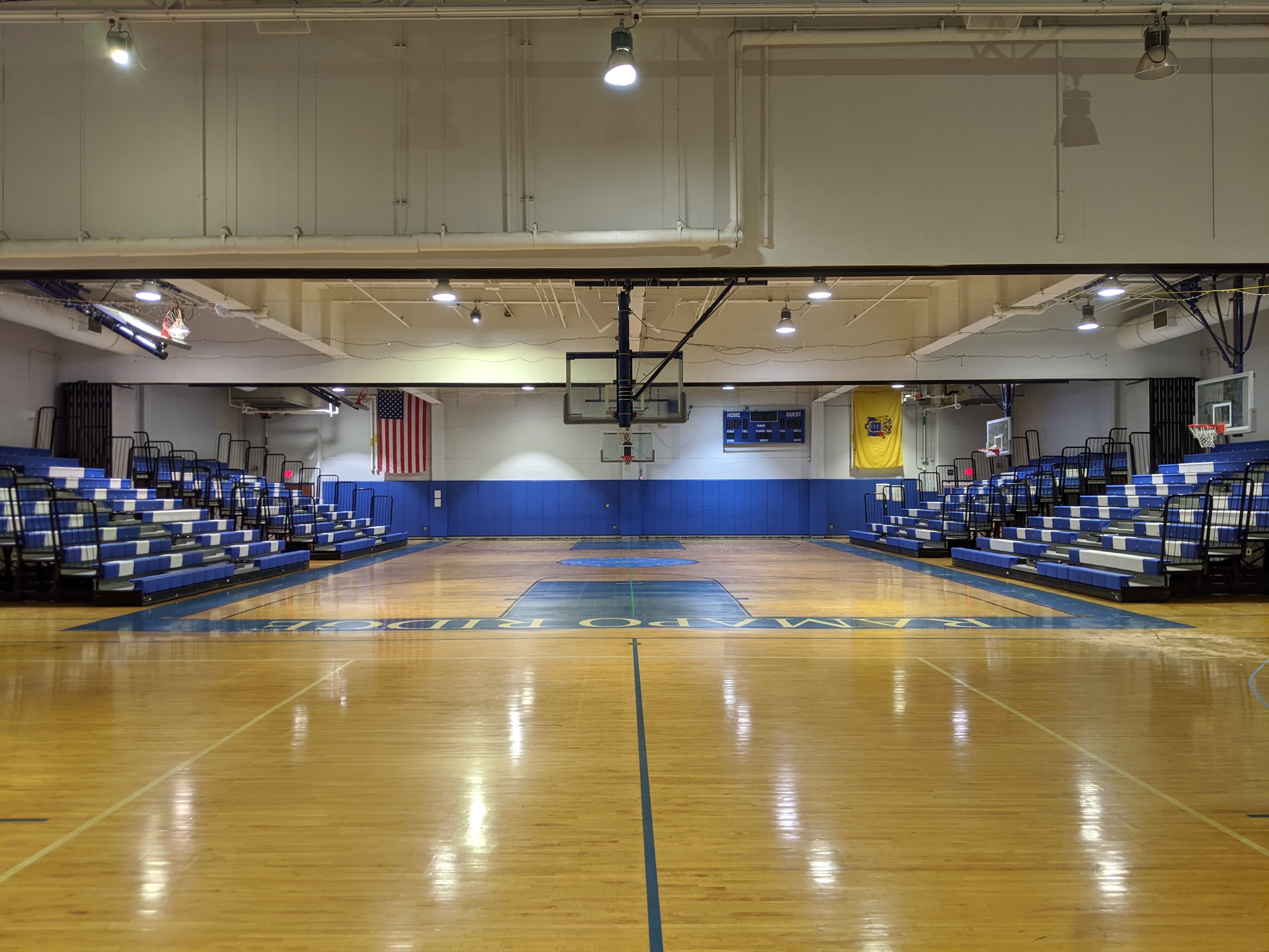 A polished wooden basketball court with blue bleachers and an American flag in the background.