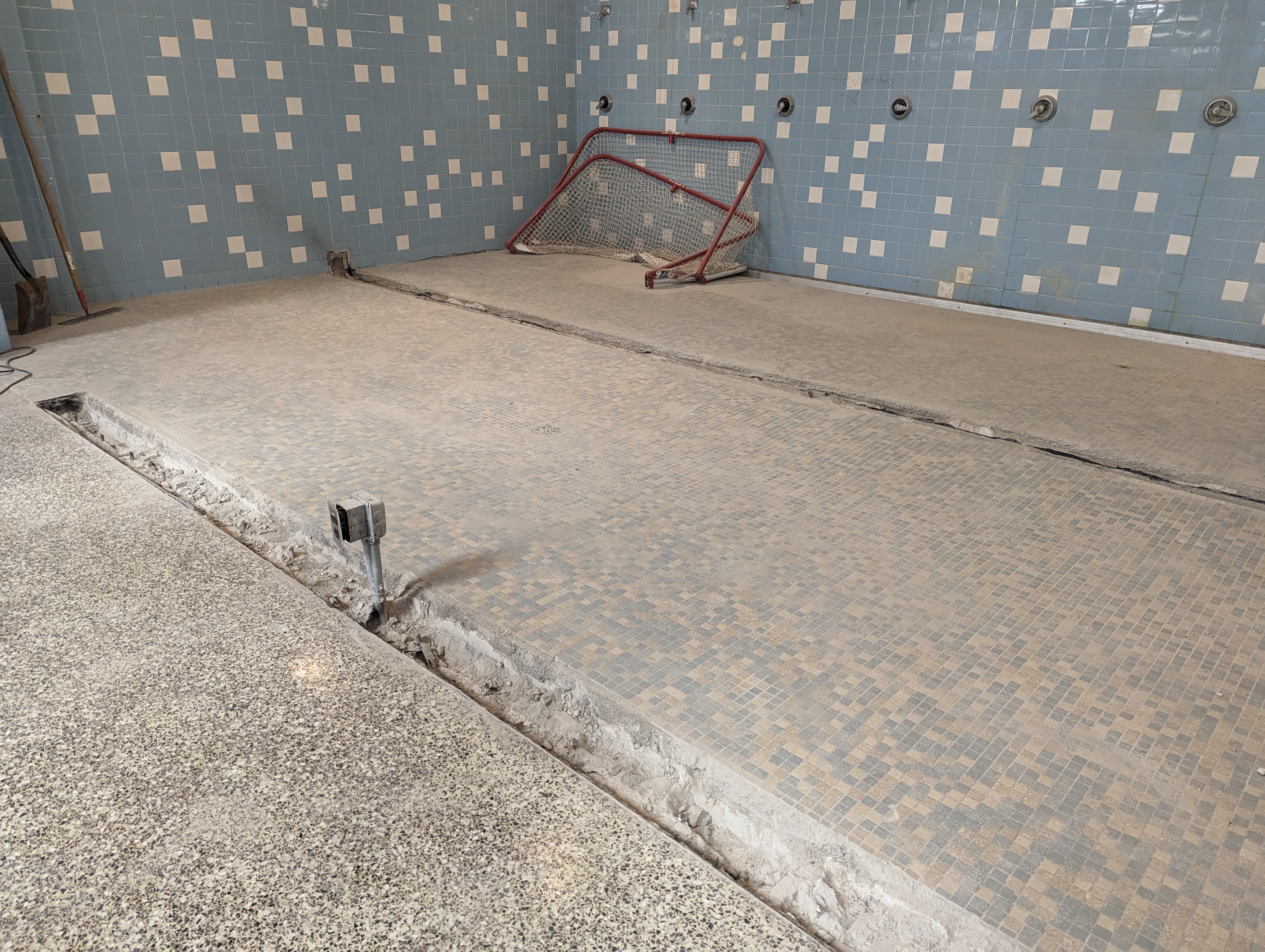 A construction site with a jackhammer in the foreground and a tiled wall in the background.
