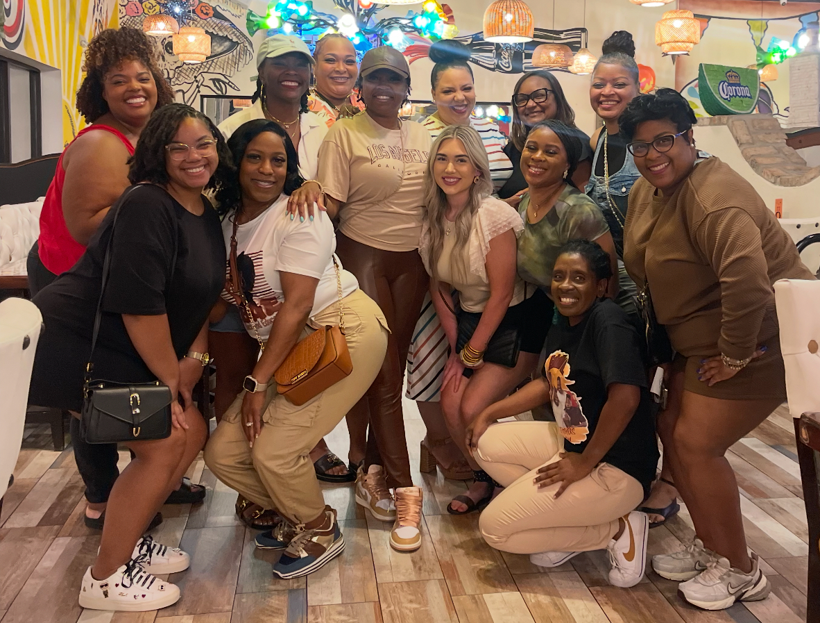 A group of women pose for a photo in a restaurant with colorful murals on the walls.