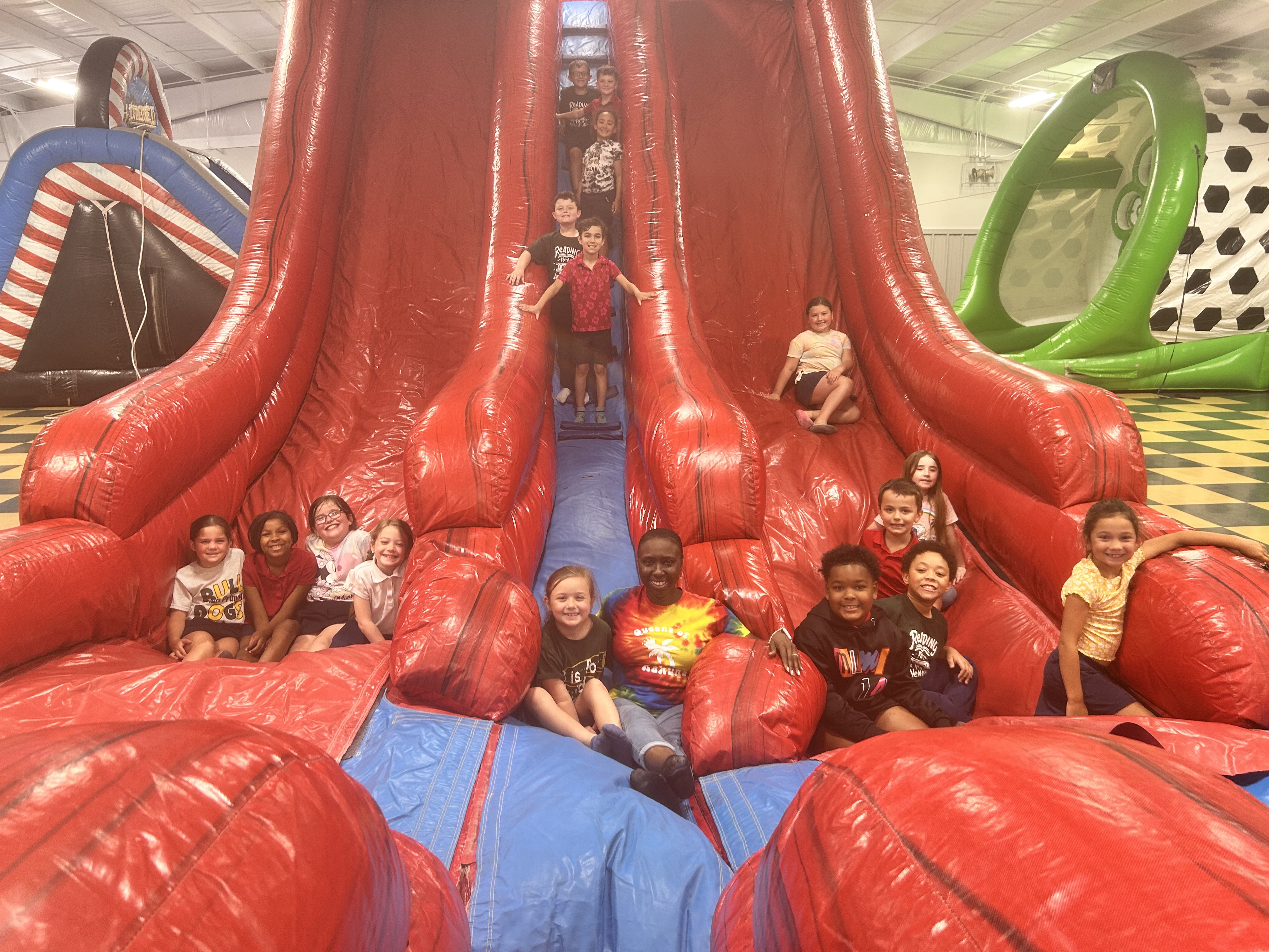 A group of children are posing on a large red inflatable slide with other colorful inflatable structures in the background.