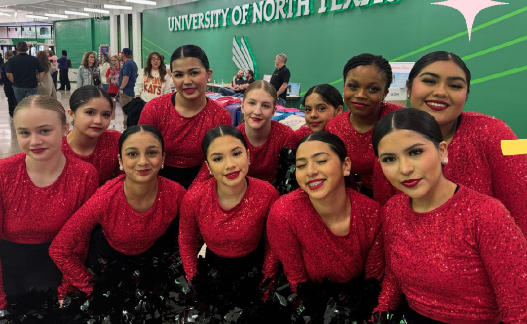 A group of young women in red sequined costumes stand together in front of a large green banner displaying the "University of North Texas" logo.