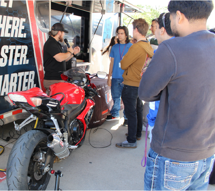 A group of people gathered around a red motorcycle, with a "Monster Starter" sign visible in the background.
