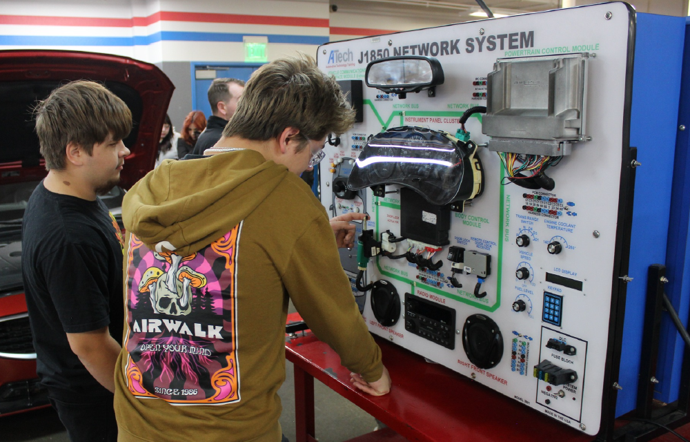 The image shows two young individuals examining a large network system display, surrounded by various electronic equipment and a colorful background.