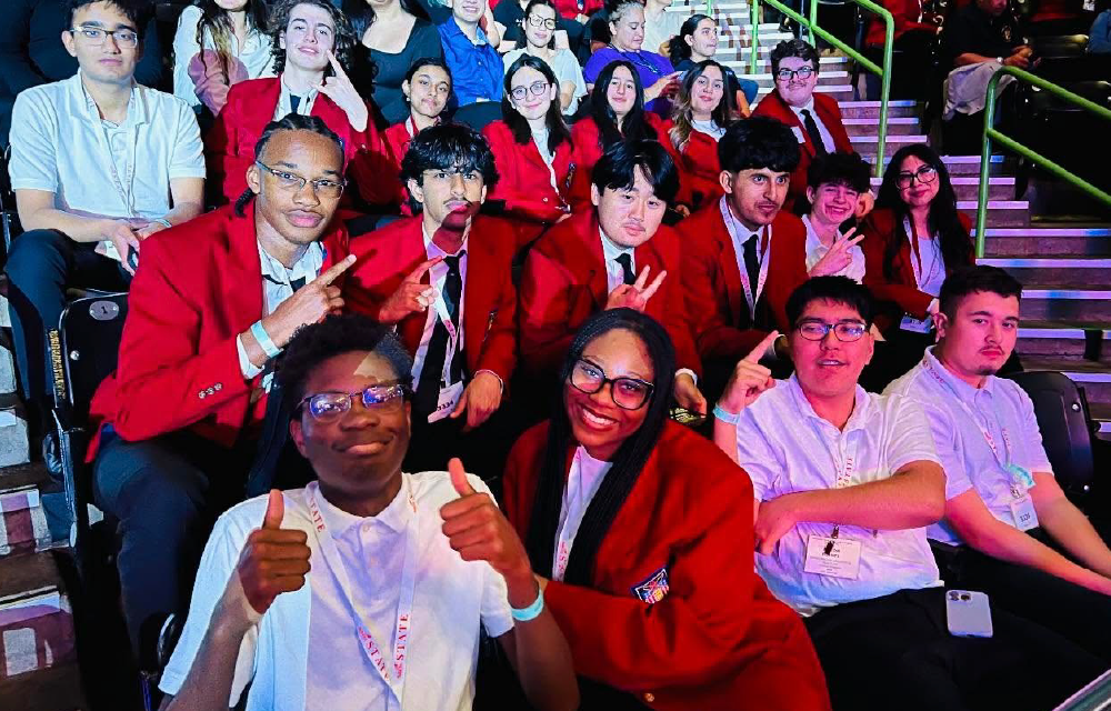 A group of people wearing red robes and smiling, standing on a stage with a colorful background.