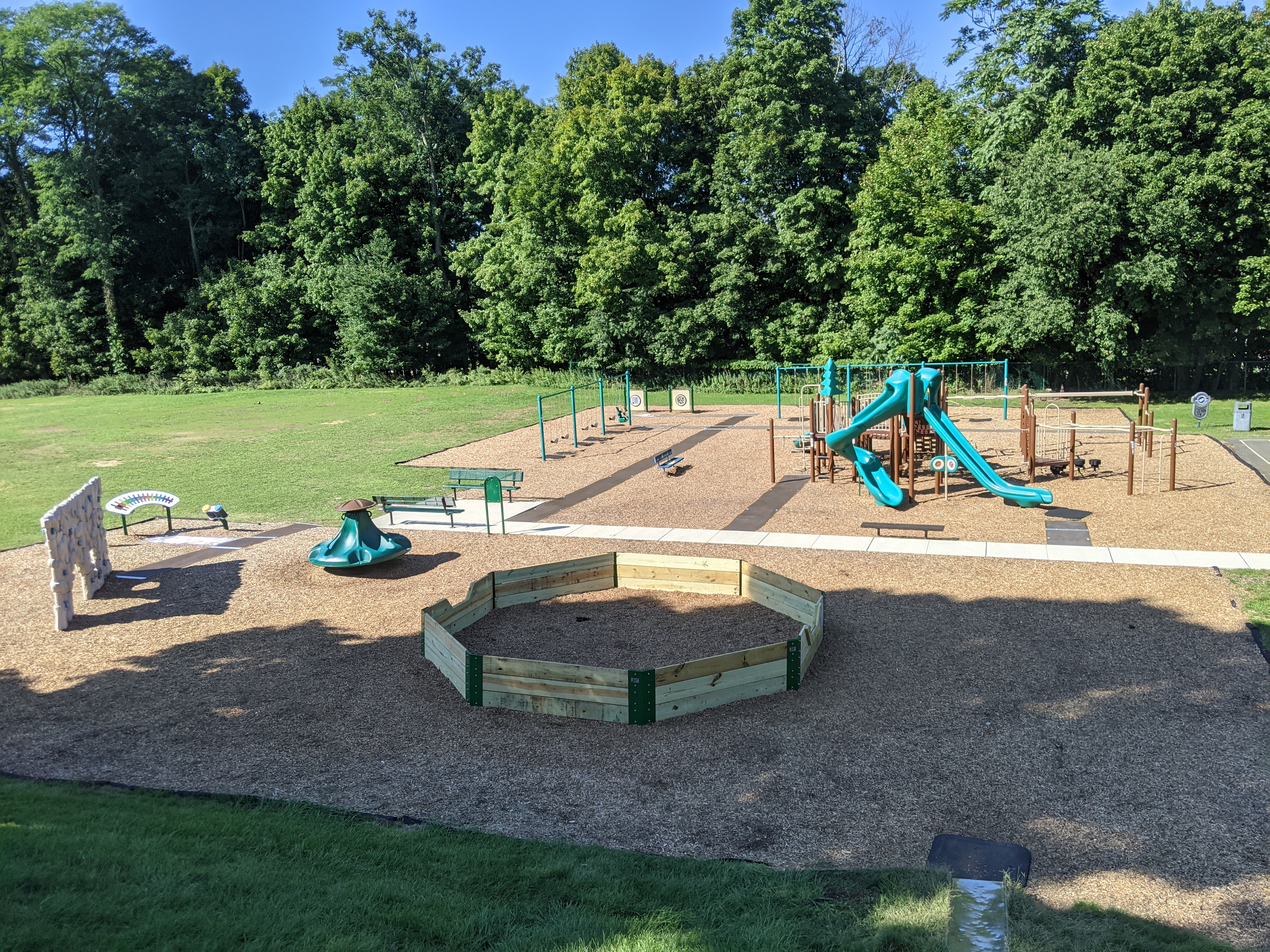 A playground with a merry-go-round and climbing structure in the foreground is set against a backdrop of lush green trees.