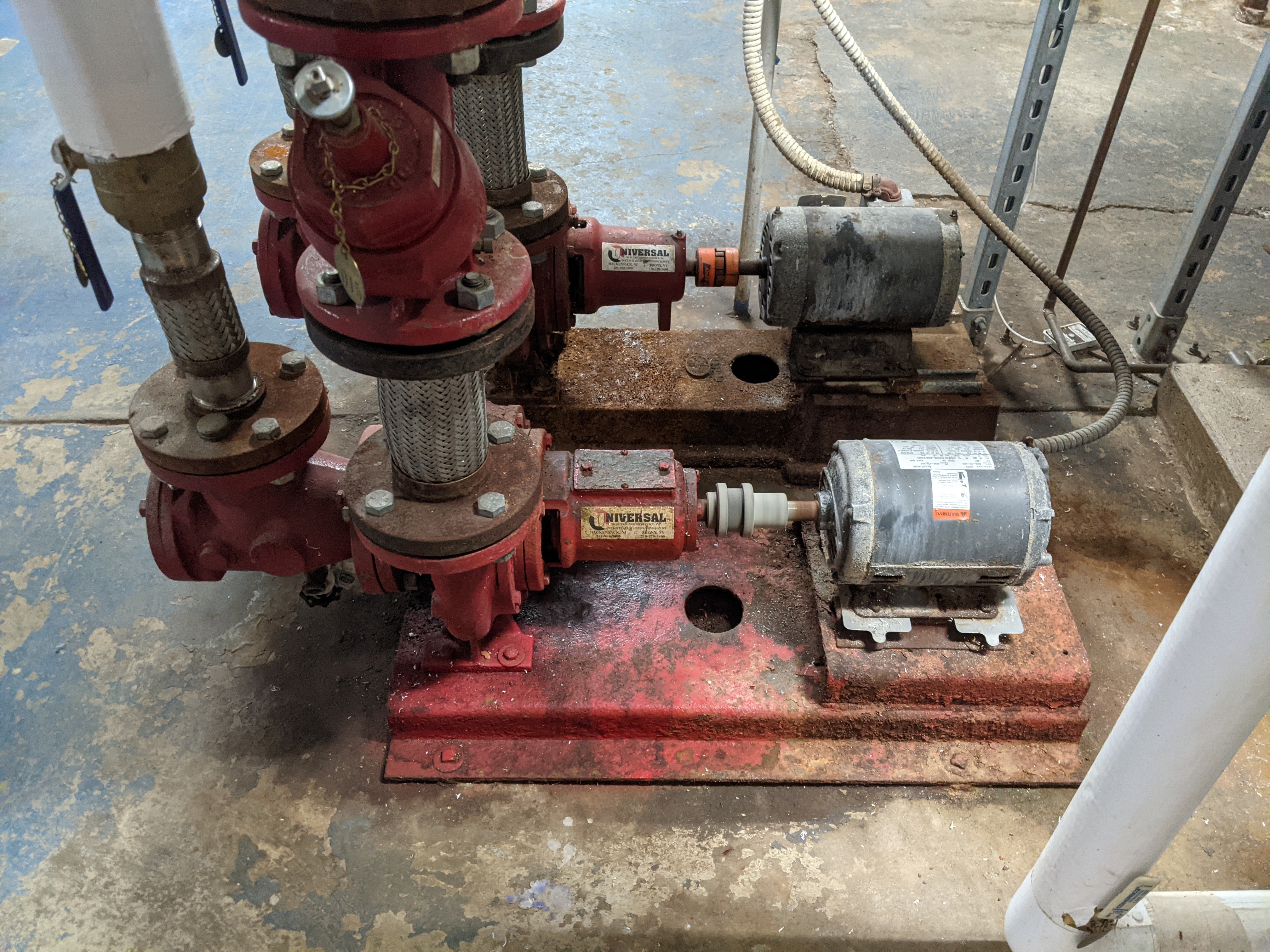 Two red industrial pumps with electric motors are in the foreground, with pipes and a metal support structure in the background.