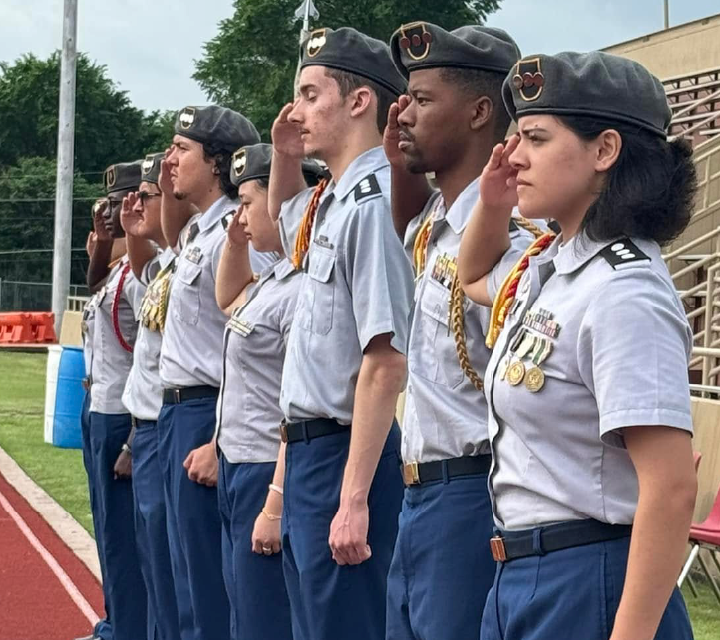 A group of uniformed individuals, likely members of a military or paramilitary organization, standing in a line on what appears to be a sports field or training ground.