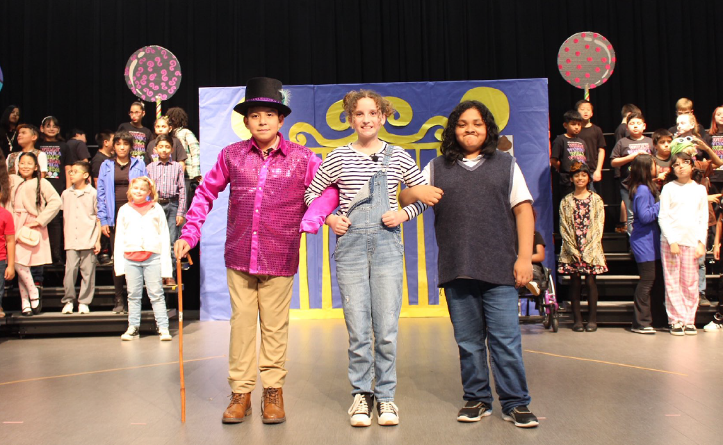 The image shows a group of people, including three individuals in the foreground, standing on a stage with a colorful backdrop.