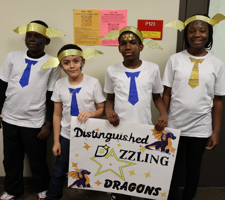 The image shows a group of four individuals wearing white t-shirts with blue ties, standing in front of a wall with various posters and signs. They are holding a banner that reads "Distinguished Dazzling Dragons".