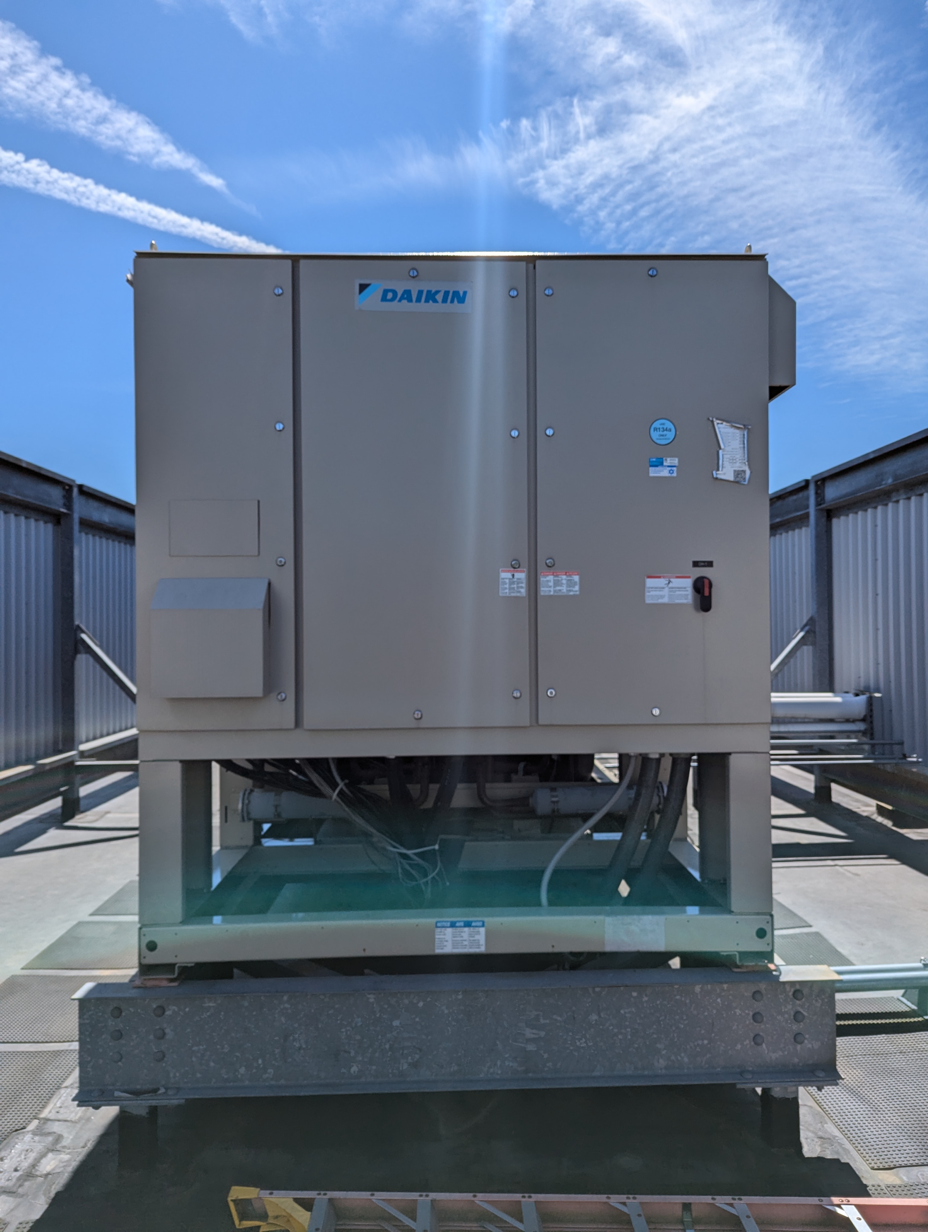 A large Daikin HVAC unit sits on a rooftop in the foreground, with a clear blue sky and wispy clouds in the background.