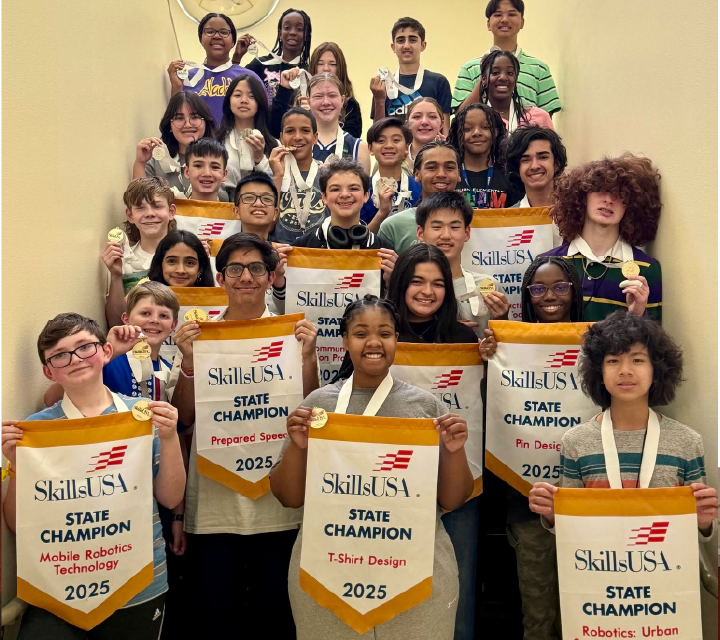 A group of diverse individuals, including both adults and children, are holding up signs celebrating their achievement as state champions in a competition related to skills and technology.