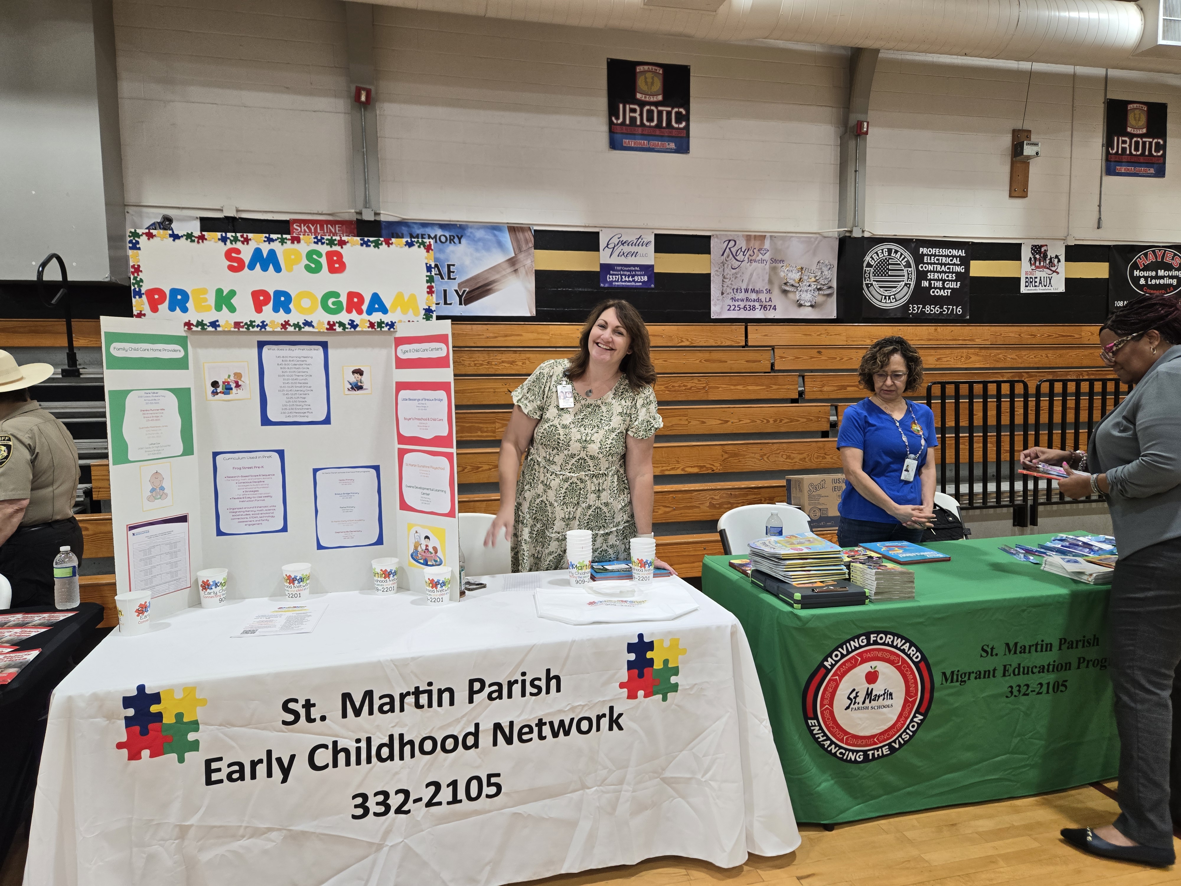 In the foreground, a table displays information for the St. Martin Parish Early Childhood Network, while in the background, a JROTC banner hangs above a gymnasium setting.