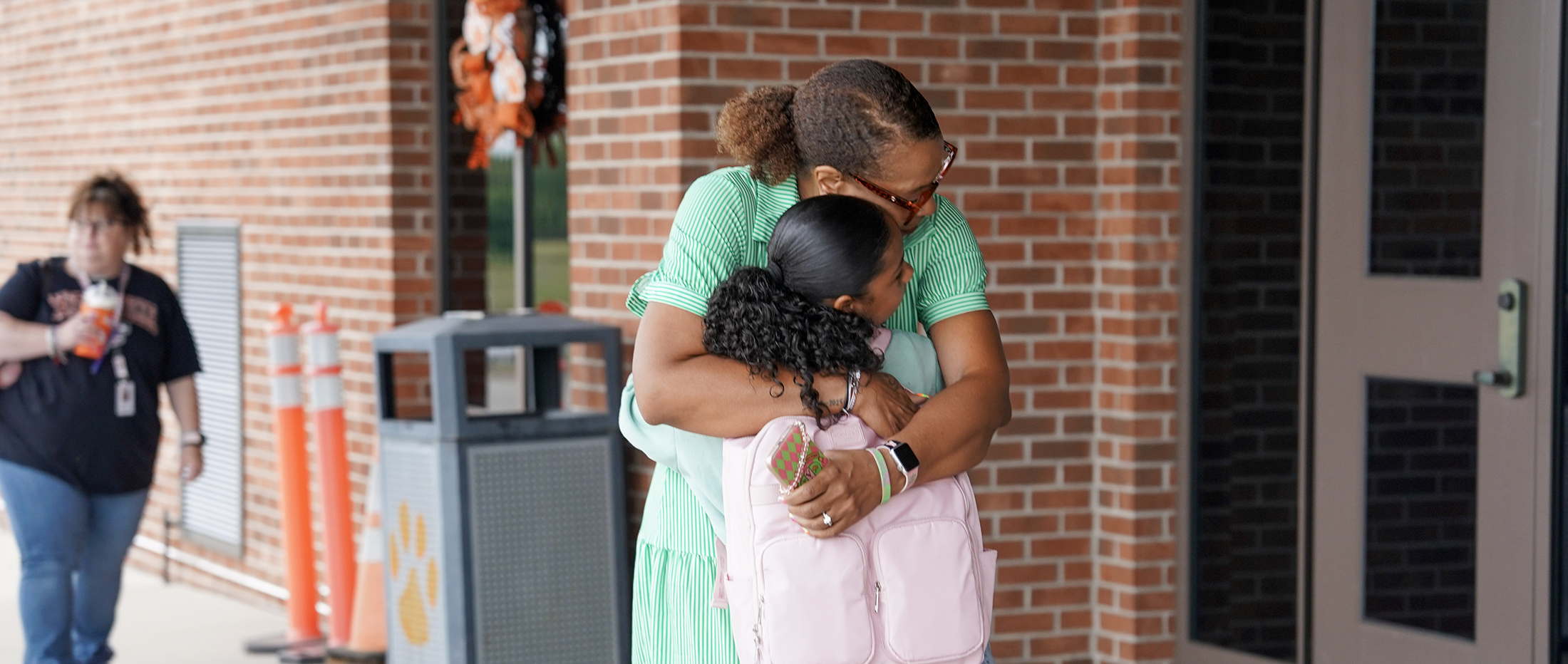 female in green dress hugs middle school student outside school building