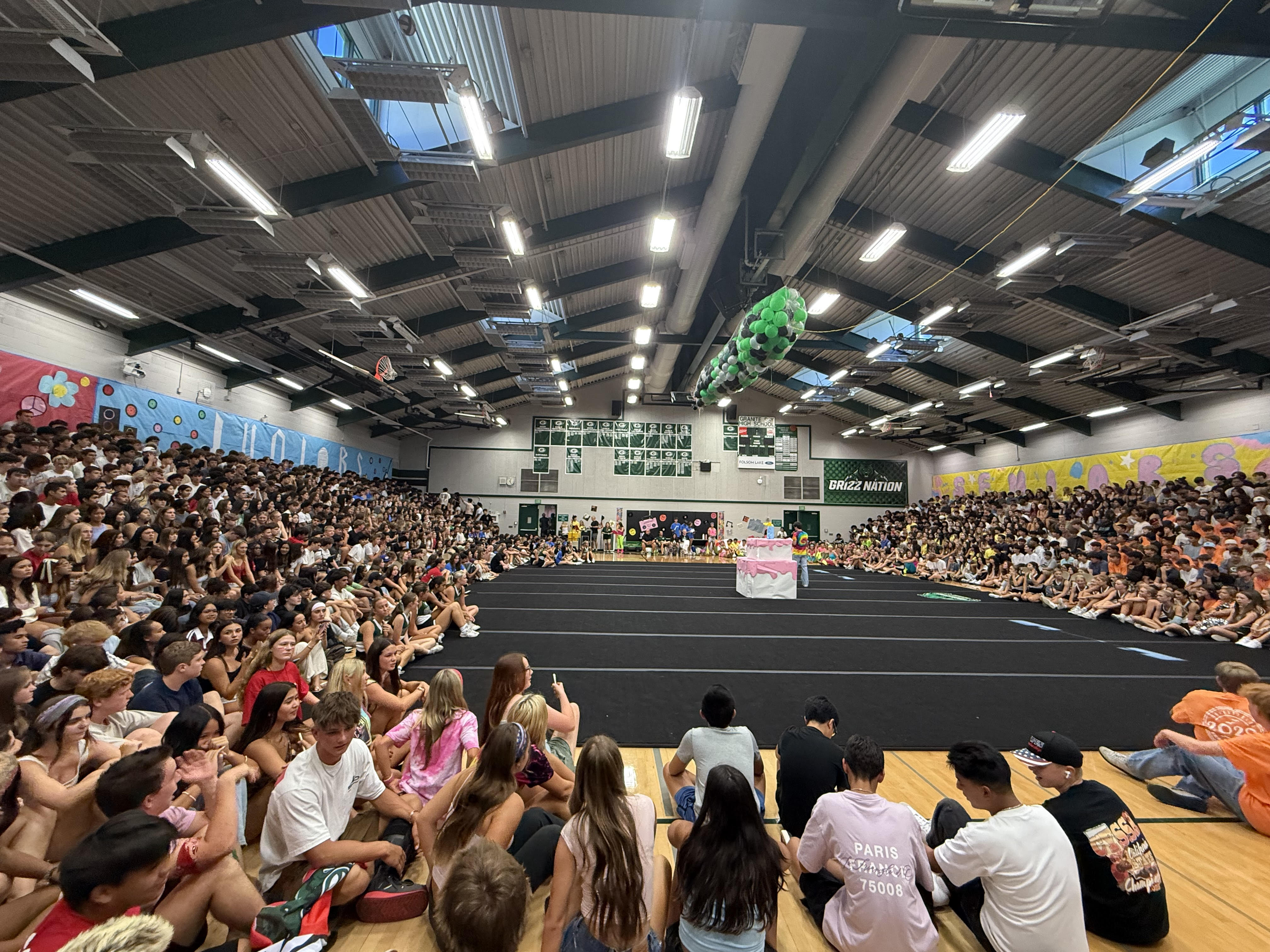 A large indoor arena filled with a crowded audience, with a stage or performance area visible in the foreground.