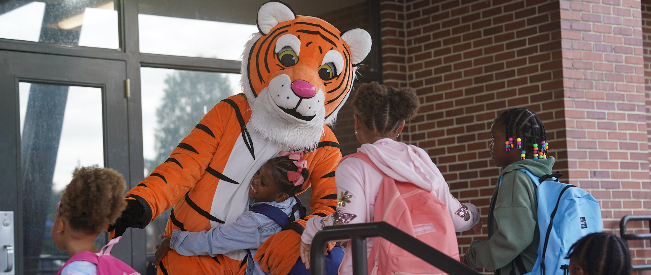 Tiger mascot hugs children on the steps of a school building