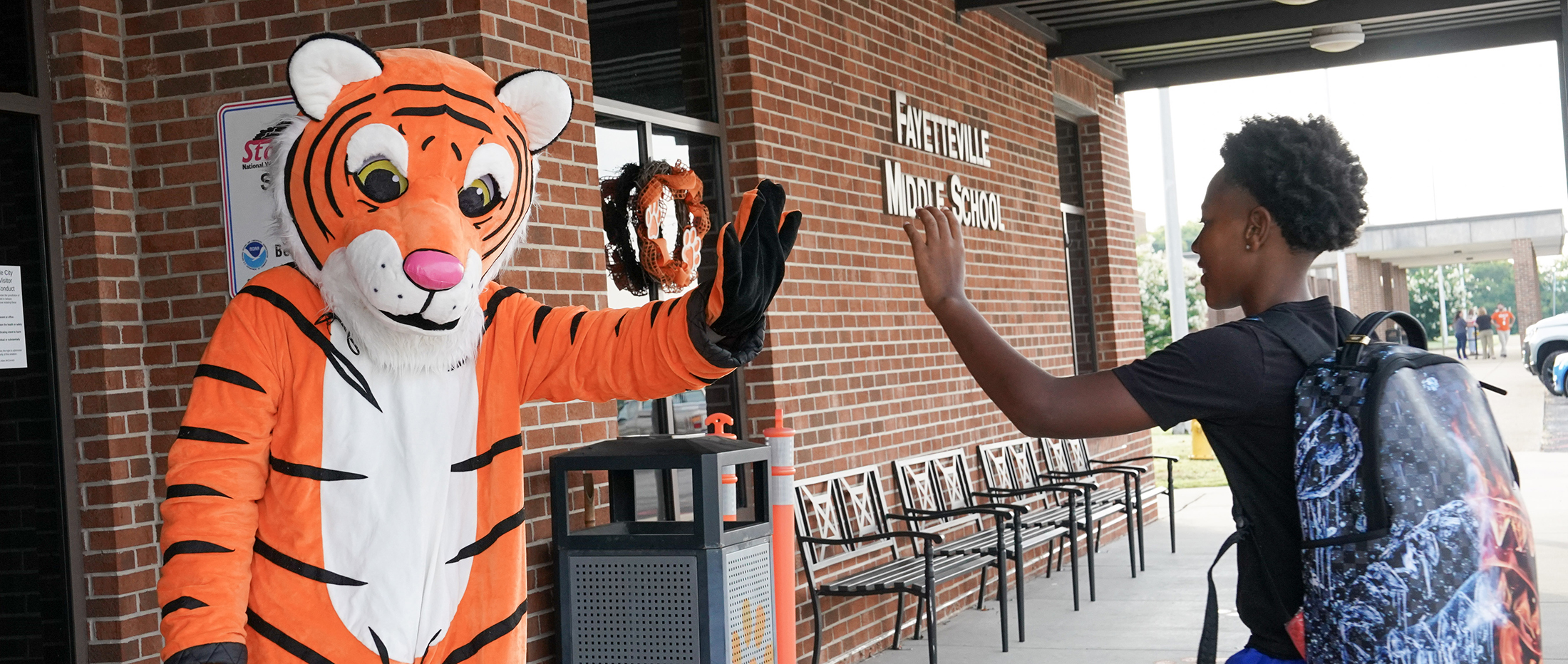 middle school student waves at Tiger mascot with Fayetteville Middle School sign in background
