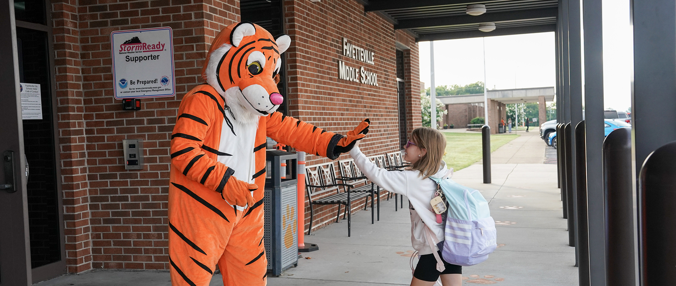 middle school student waves at Tiger mascot with Fayetteville Middle School sign in background