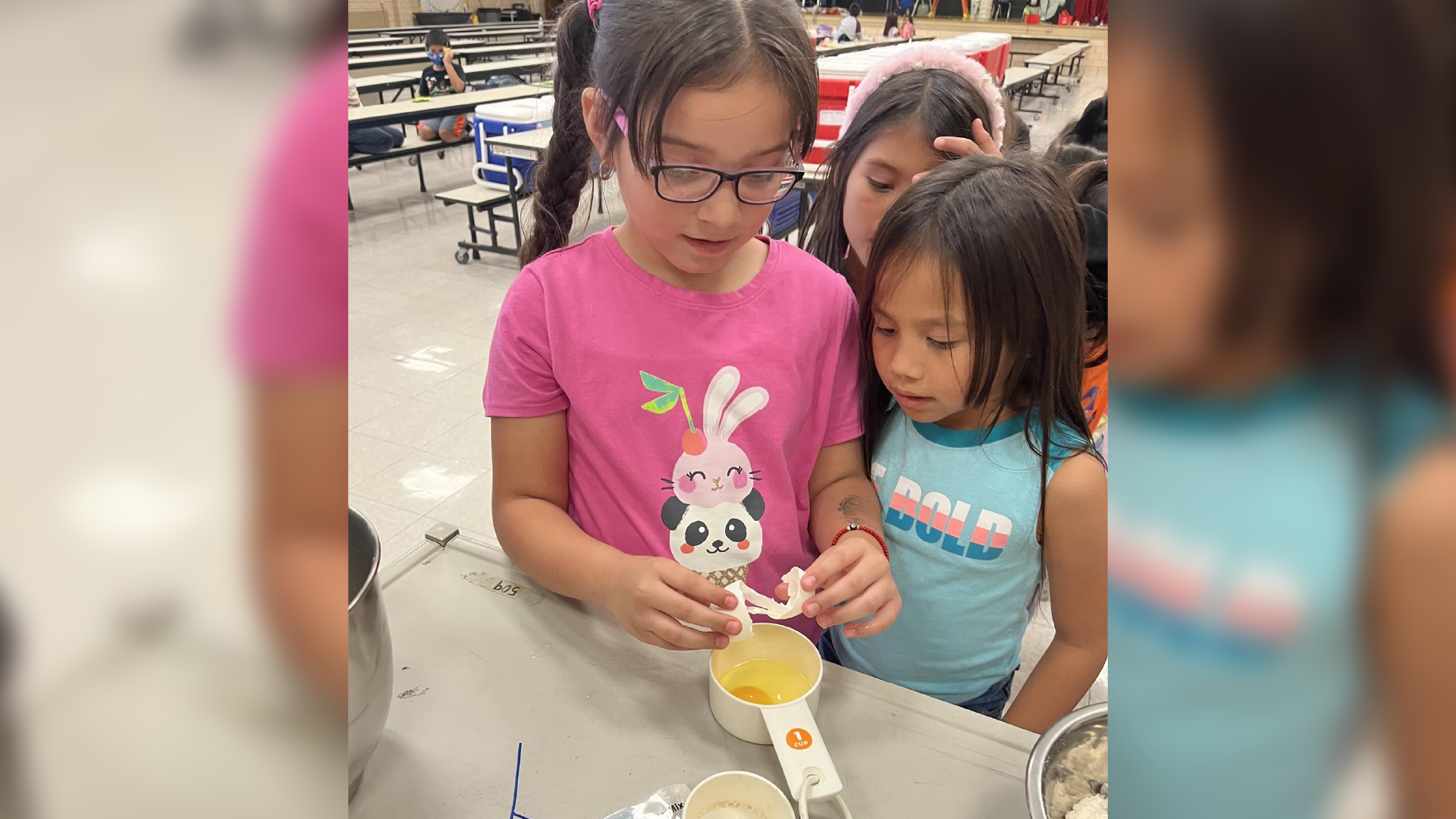 Two young children, a boy and a girl, are standing in what appears to be a classroom or educational setting, engaged in an activity or project together.
