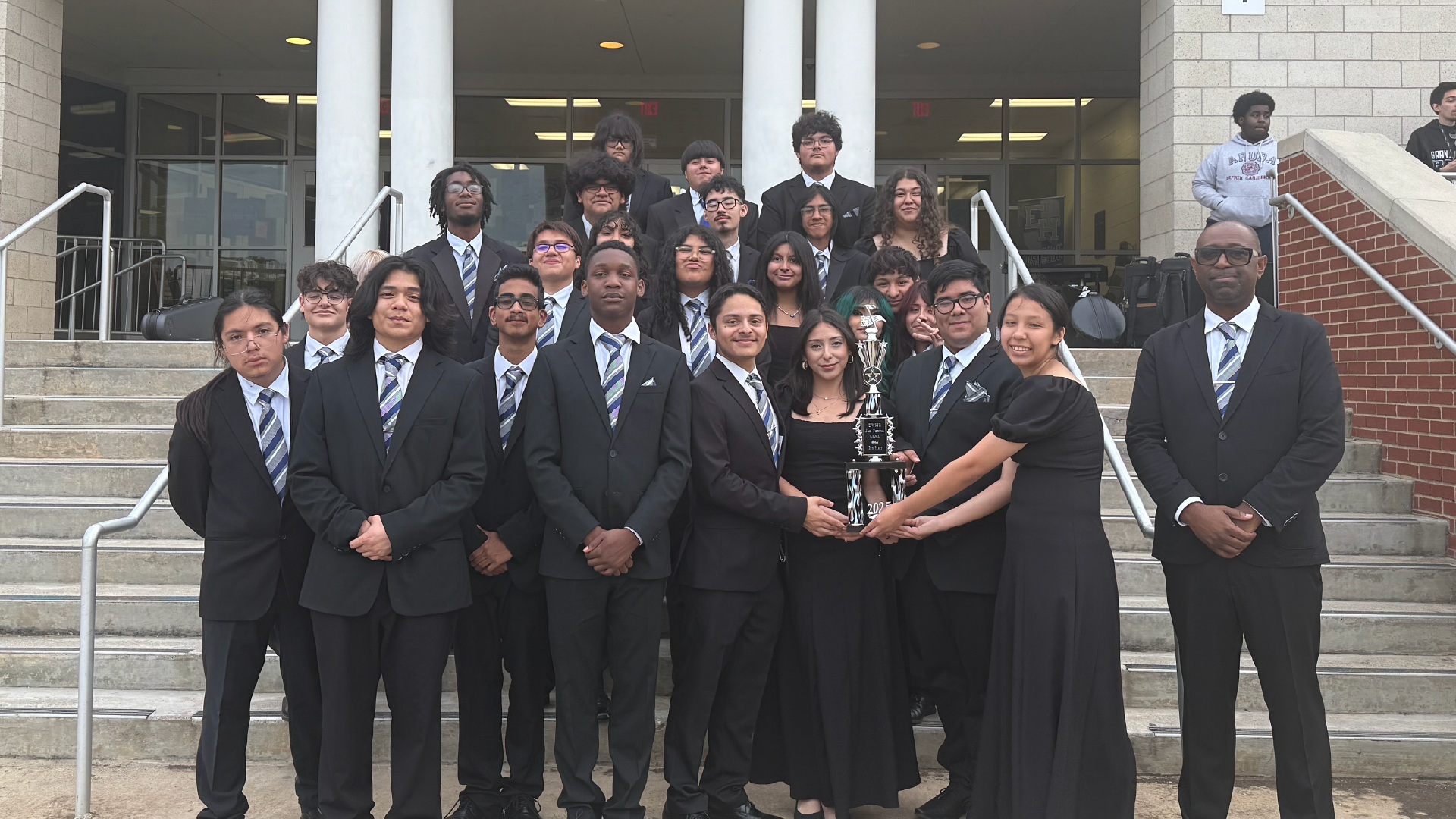 A group of people, likely students, dressed in formal attire standing on the steps of a building.