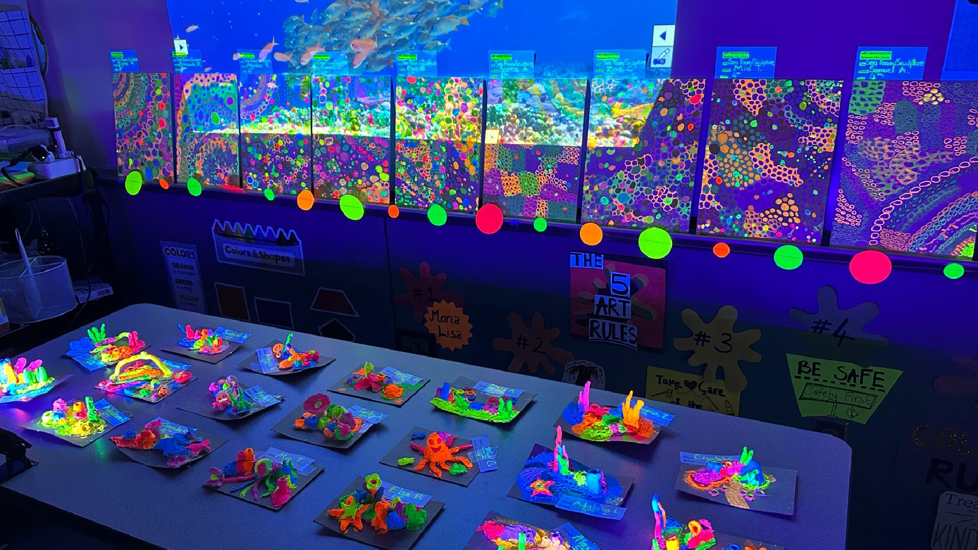 A vibrant and colorful display of fluorescent artwork, including various shapes and patterns, illuminated under a black light against a backdrop of a nighttime cityscape.