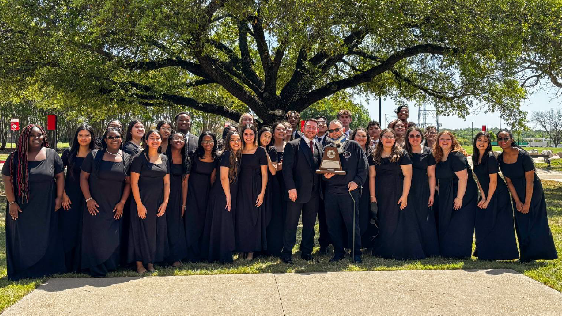 A large group of people dressed in black robes standing together in front of a lush, green tree.