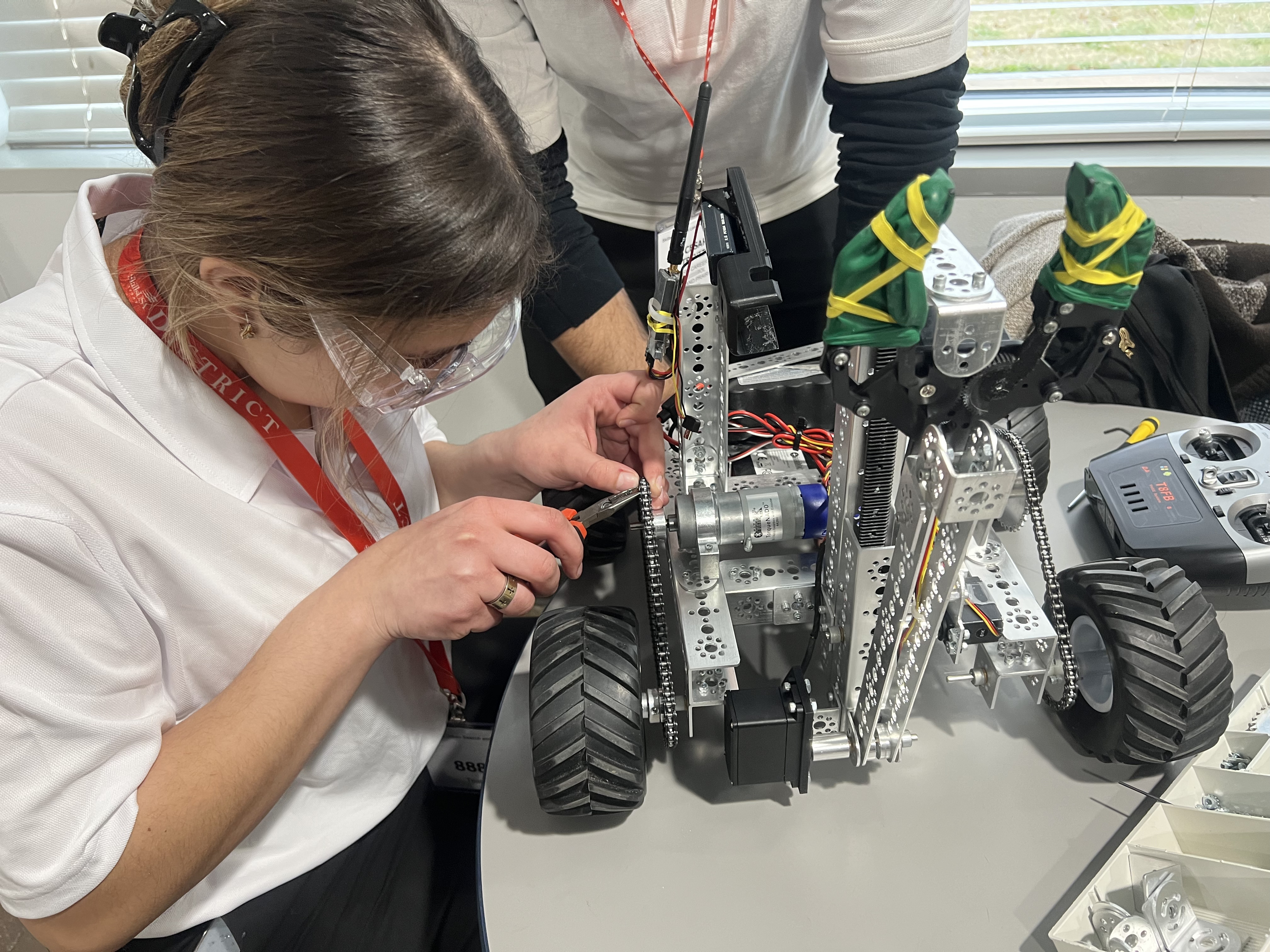 A person in a white shirt is closely examining a robotic vehicle with various components and attachments, surrounded by other robotic equipment in the background.
