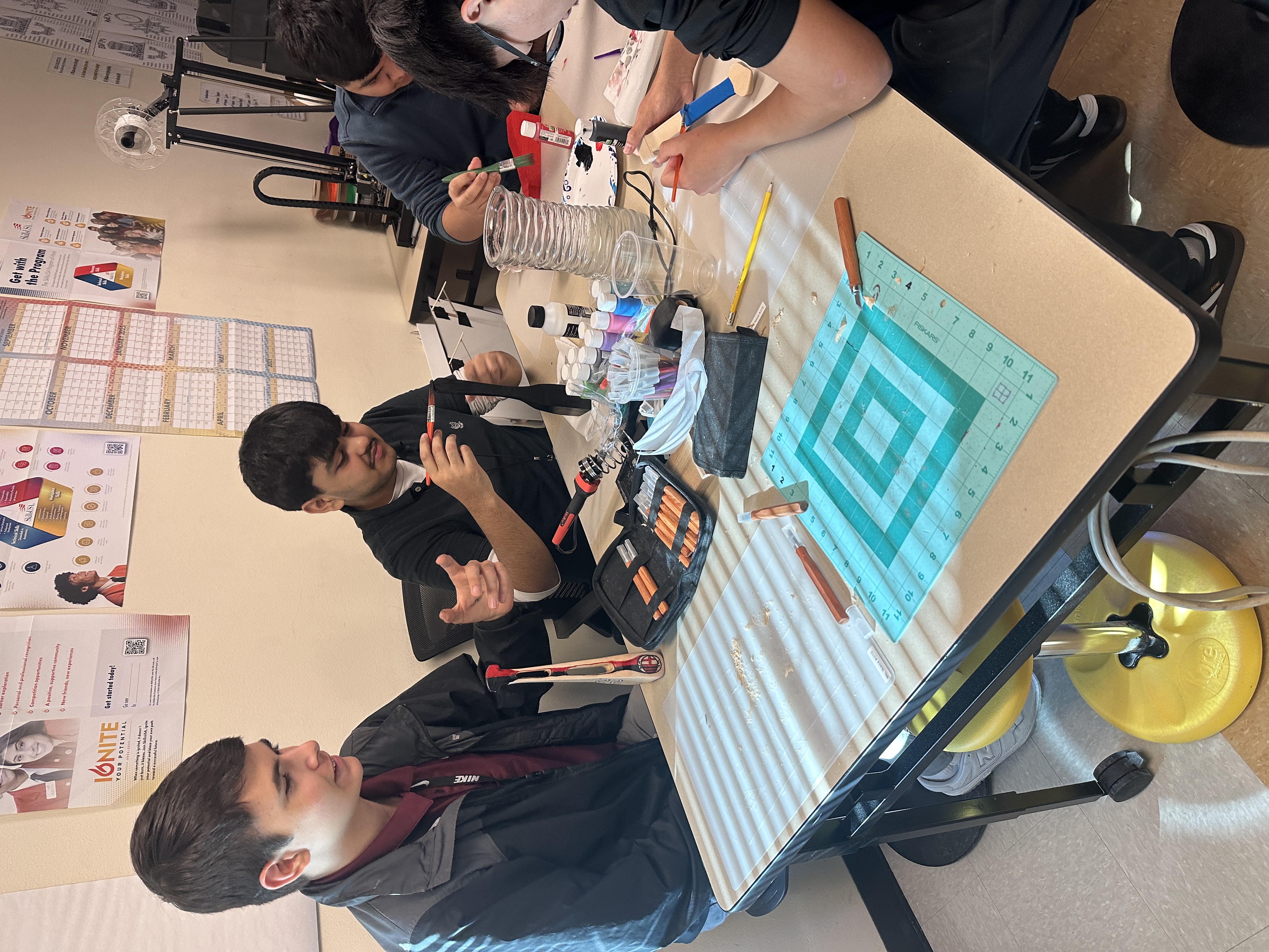 A group of students are engaged in a hands-on art project, working together at a table filled with various art supplies and materials.
