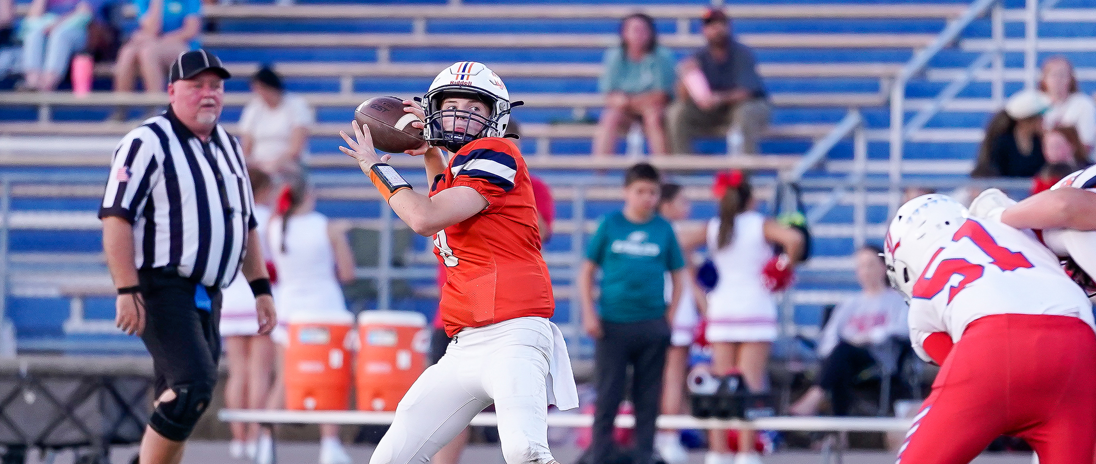 middle school quarterback in orange jersey and white pants stands in the pocket to throw the ball
