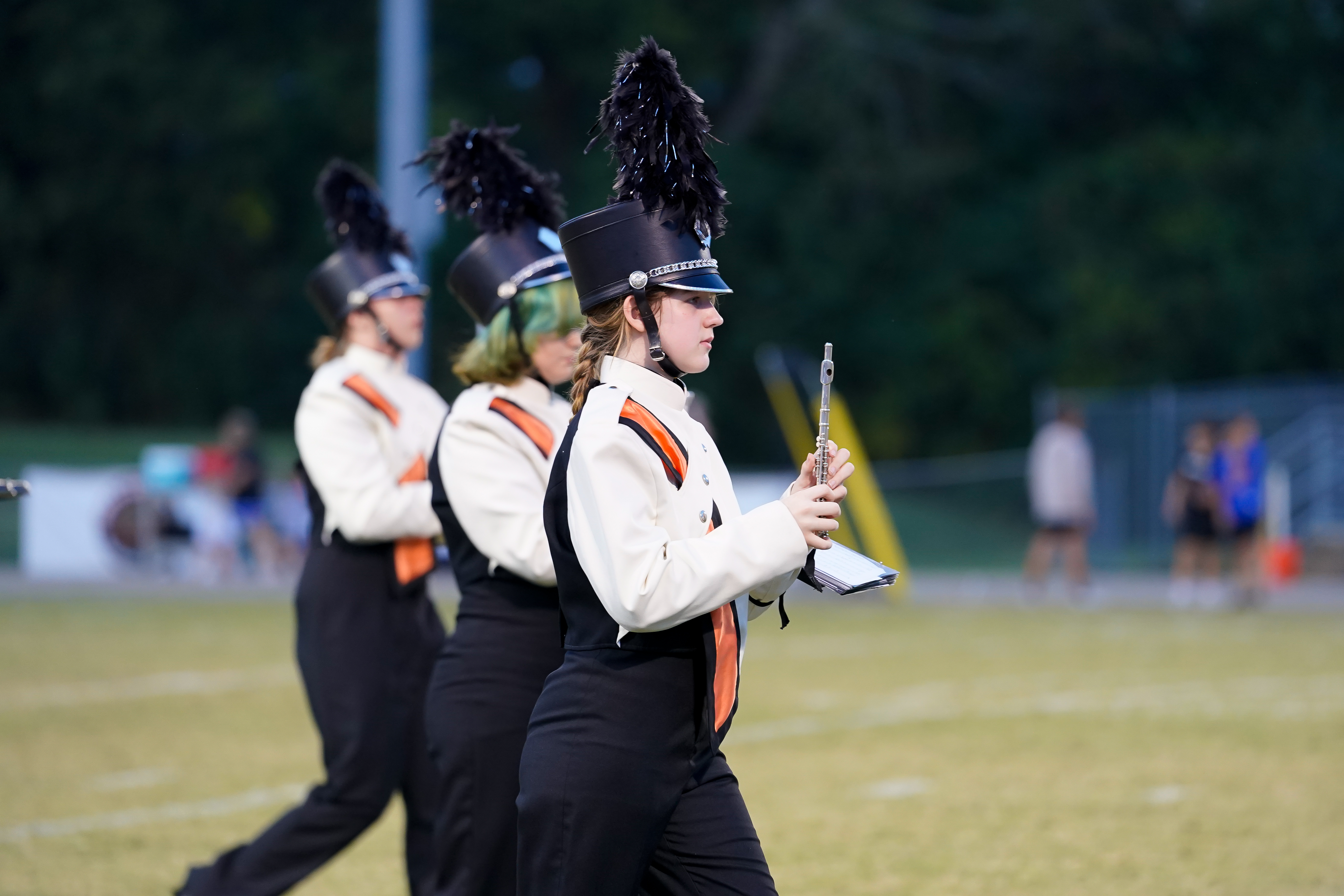 Tiger band member in white uniform marches with a flute in hand during the halftime show.