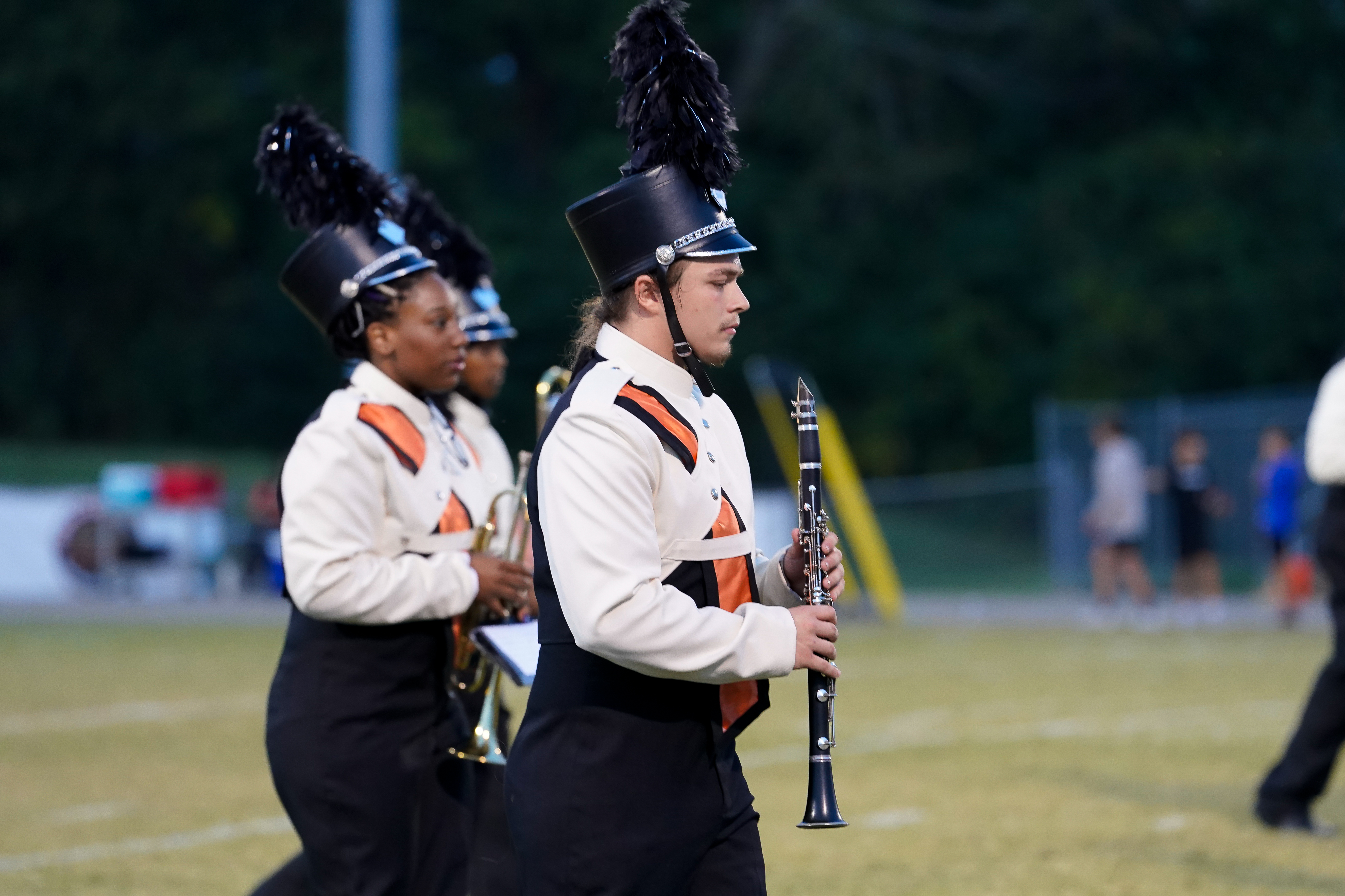 Tiger band member in white uniform holds a clarinet while marching across the field.