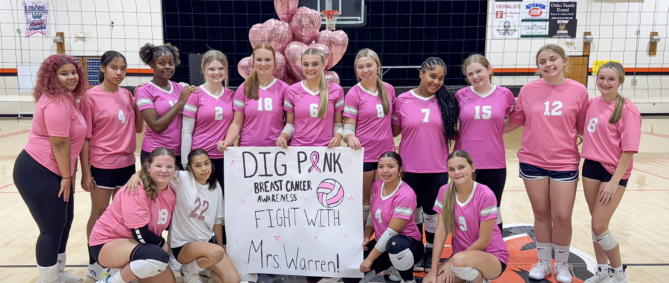 high school volleyball team in pink uniforms holding sign about Dig Pink