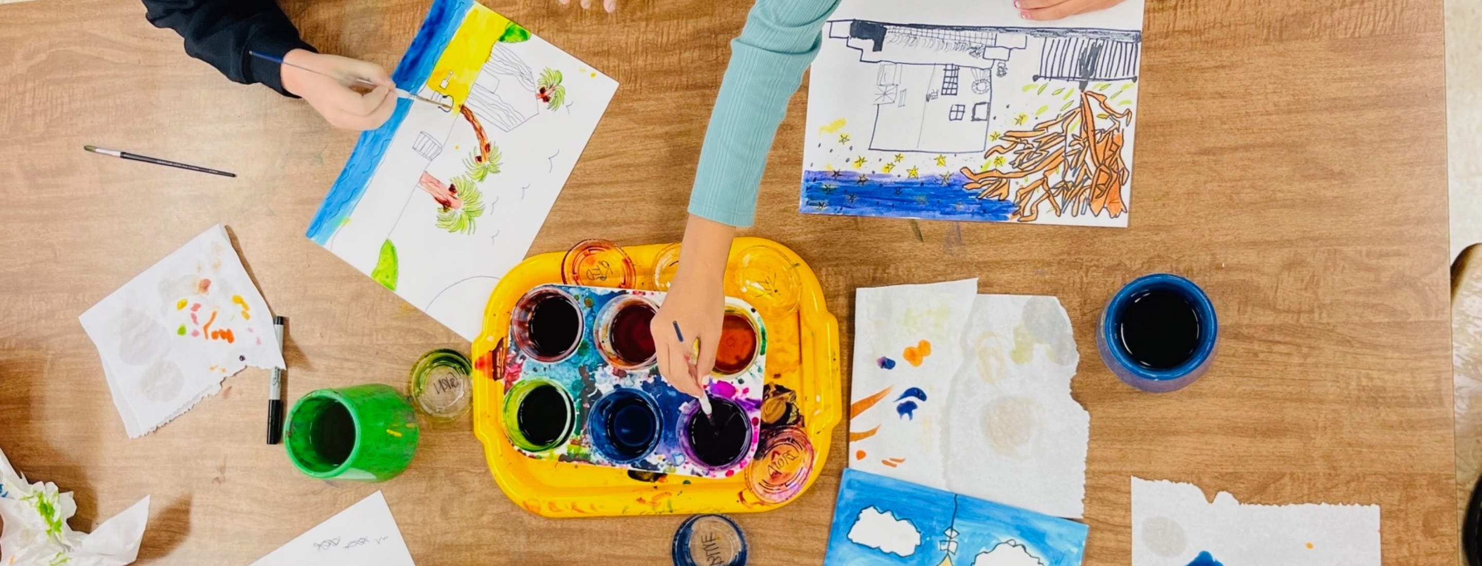 Students painting artwork on a table. 