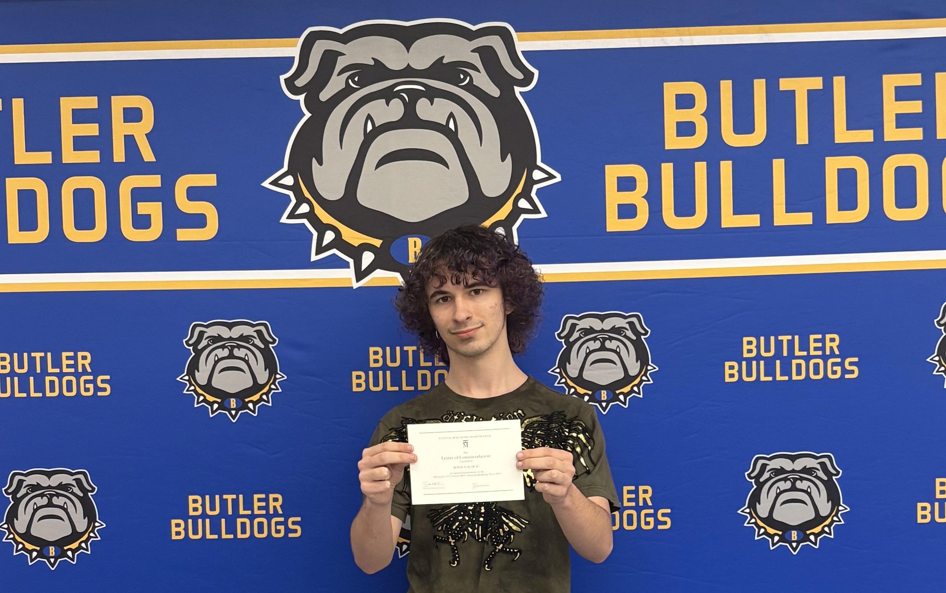 A young person with curly hair stands in front of a blue backdrop featuring the Butler Bulldogs logo and mascot.