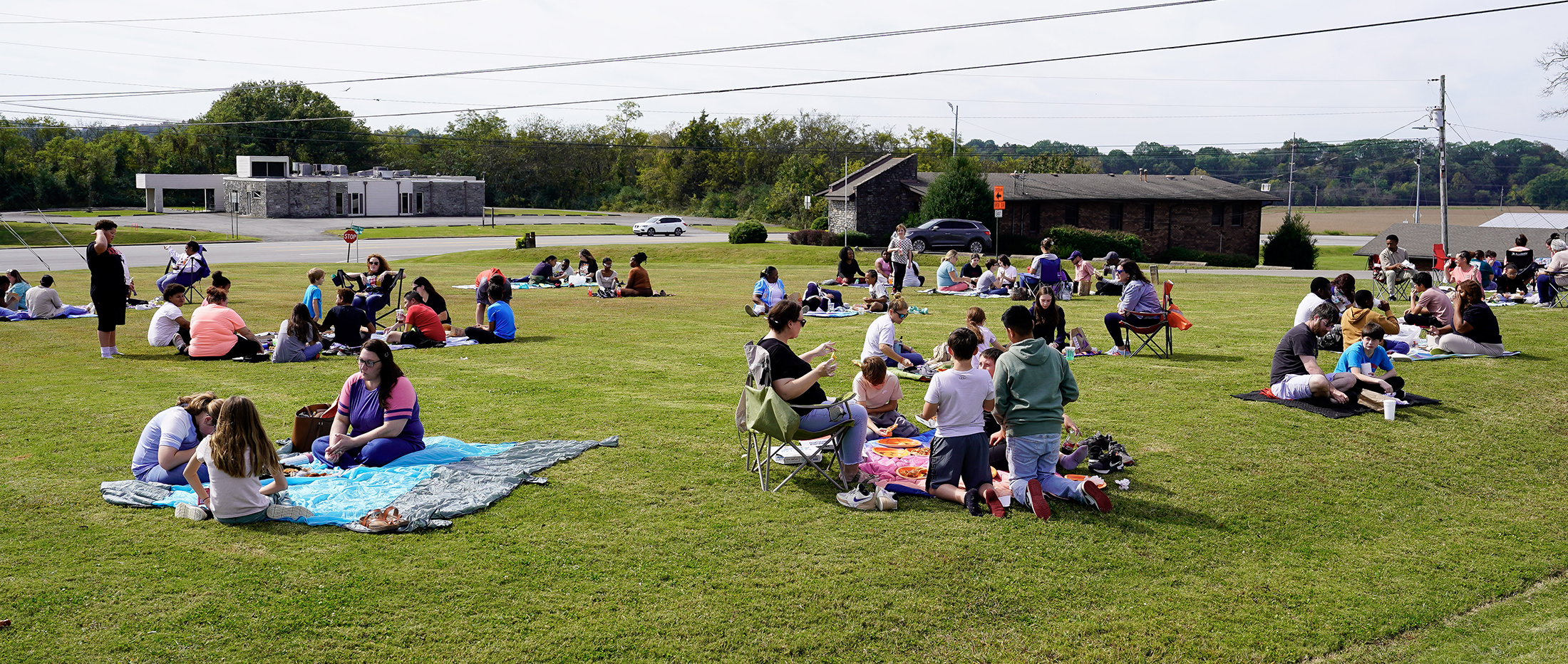 several families eating lunch seated on a green grassy field
