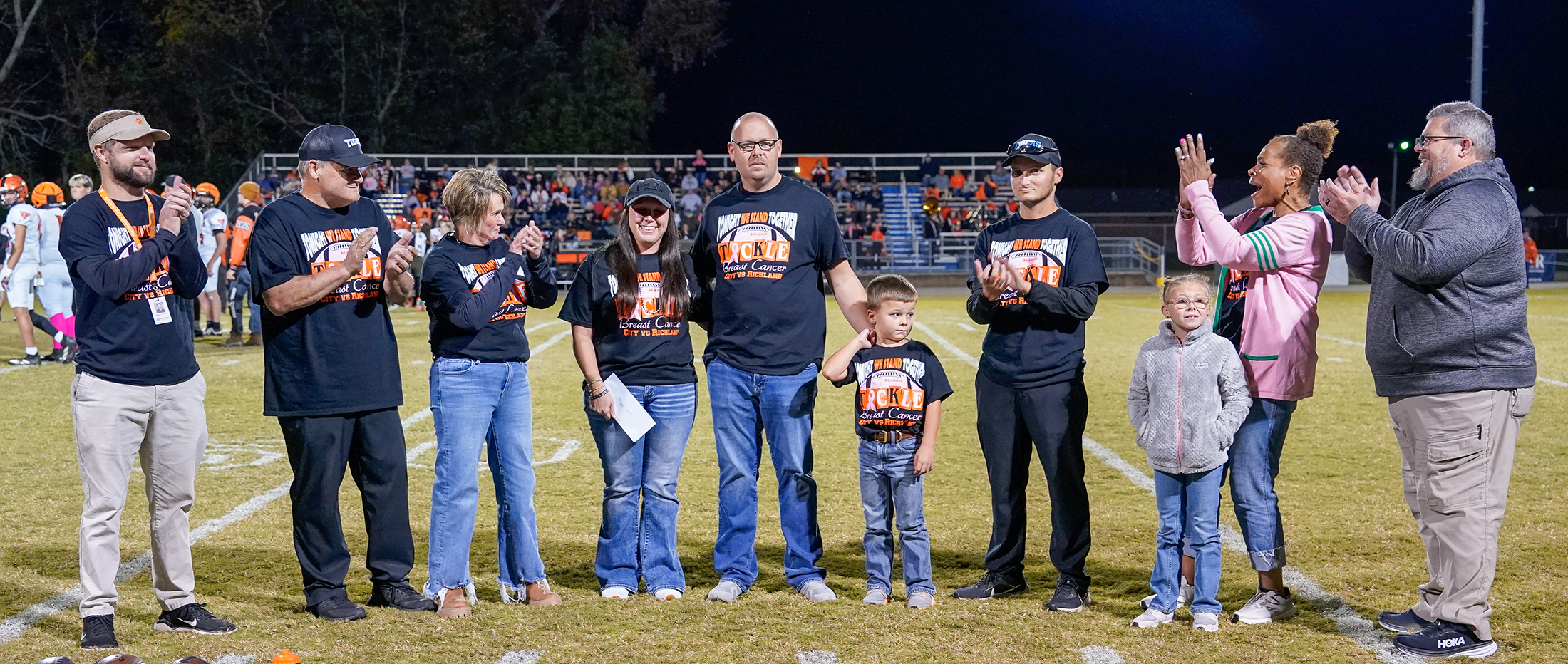 Group on the football field applauding while woman in breast cancer shirt accepts check