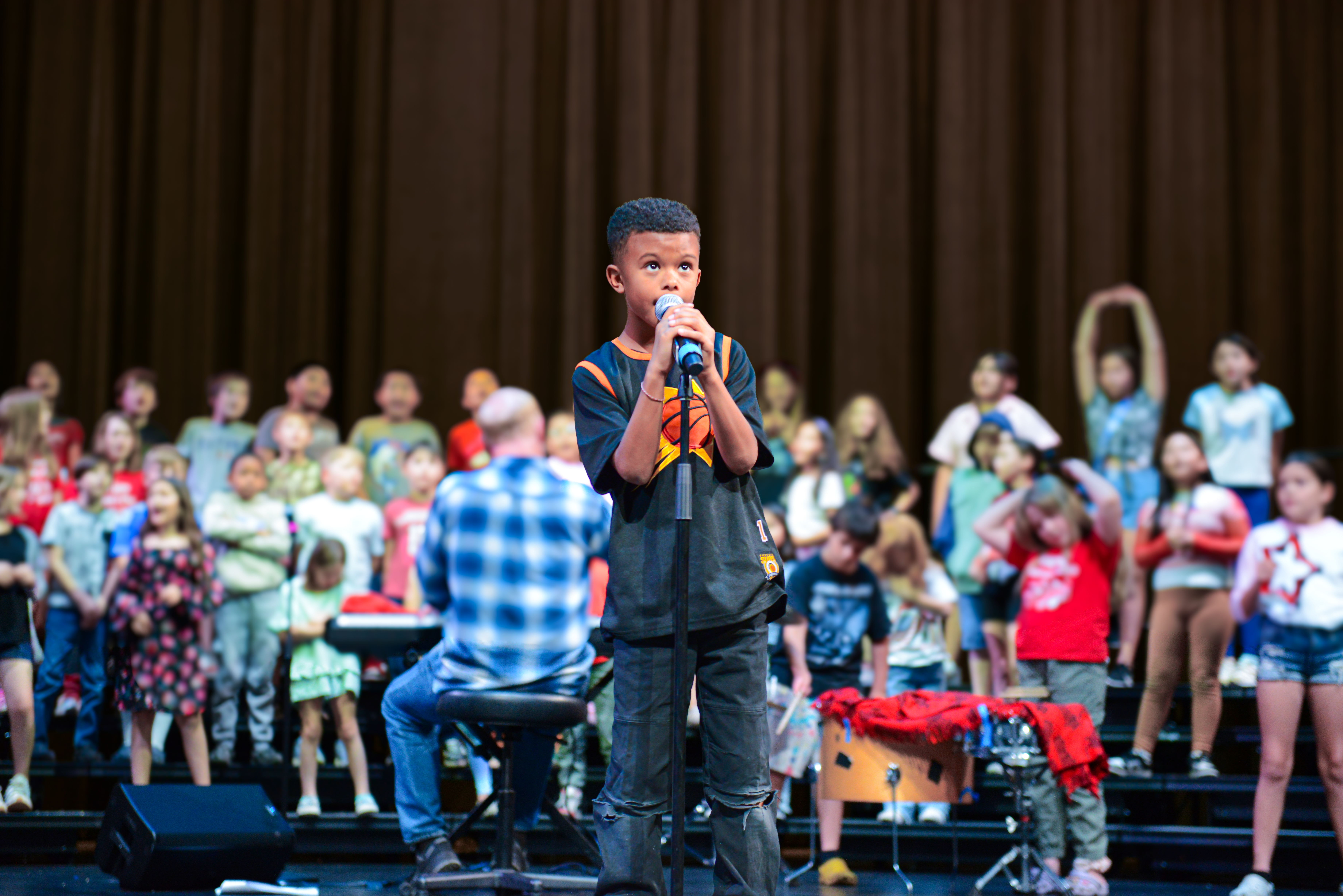 little boy singing on stage at the Madison Center for the Arts with his classmates behind him
