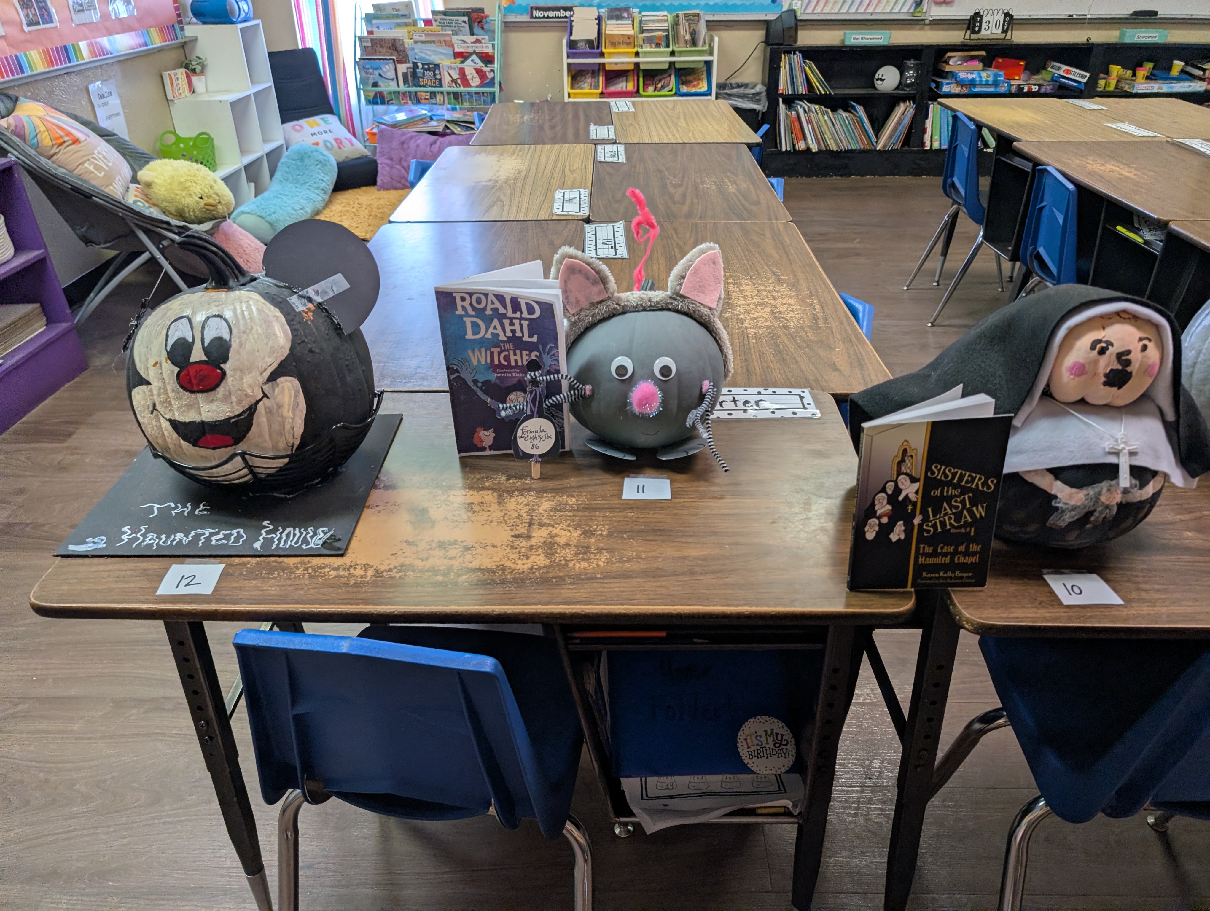 A classroom or learning space with various decorative items, including plush toys and signs, placed on a wooden table in the foreground.