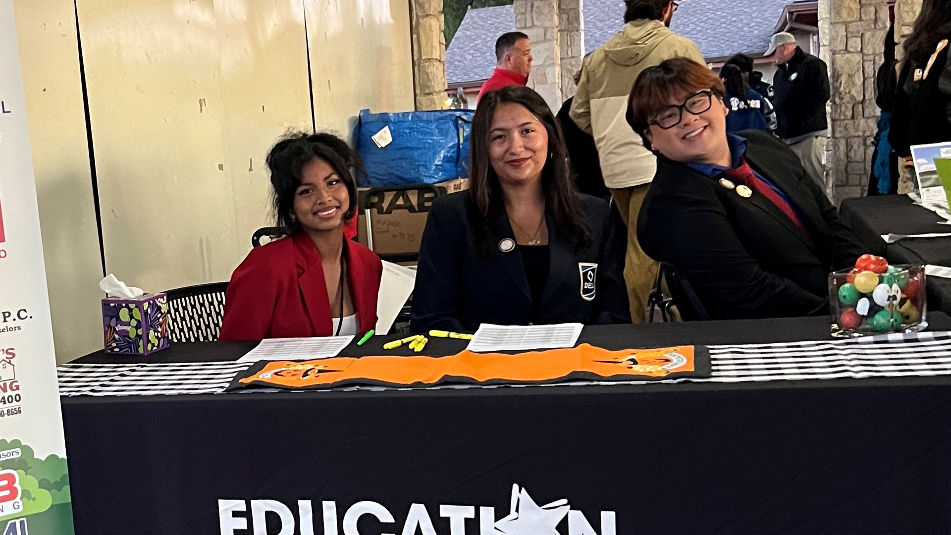 The image shows a group of people, likely educators or school staff, standing behind a table displaying various educational materials and decorations.