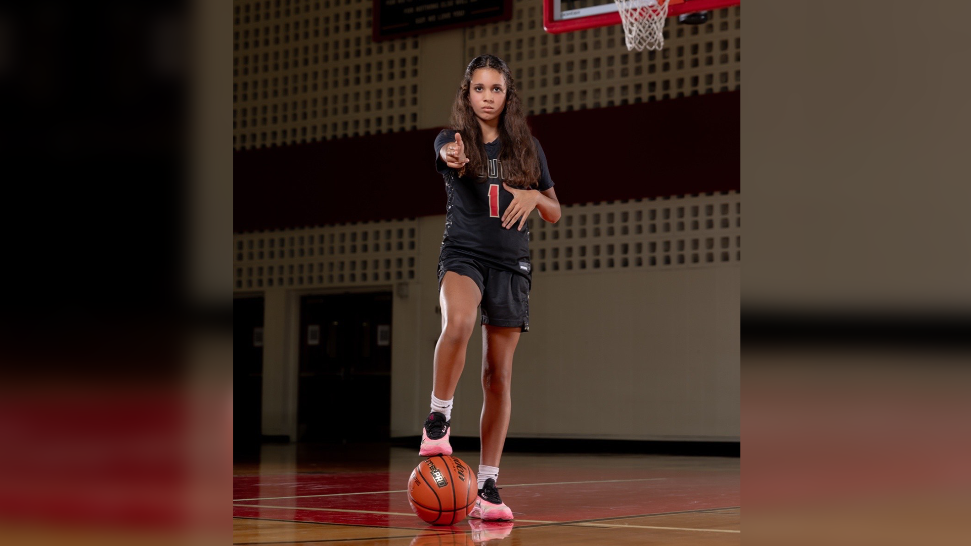 A young woman in athletic clothing stands on a basketball court, holding a basketball and appearing ready to play.