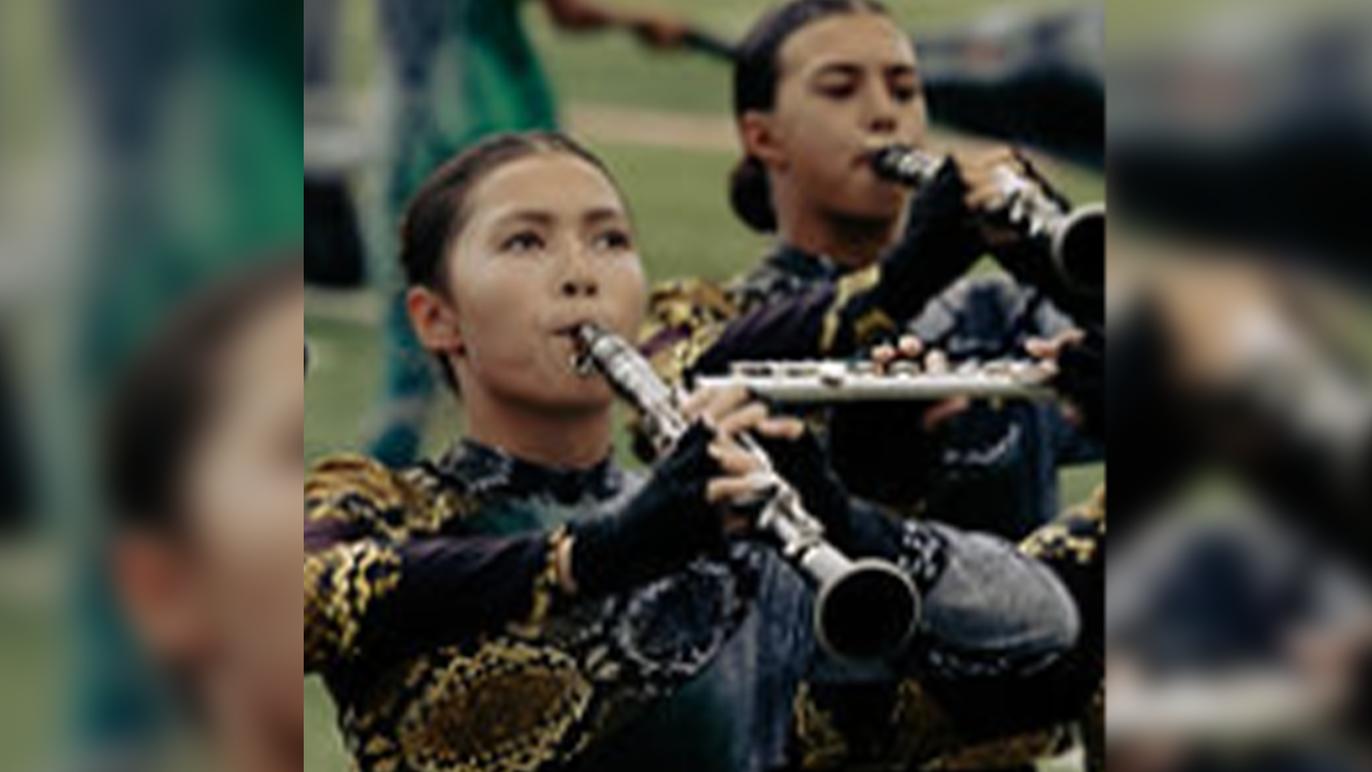 Two individuals, a man and a woman, are playing musical instruments, likely wind instruments, on a stage or performance setting with a blurred background.