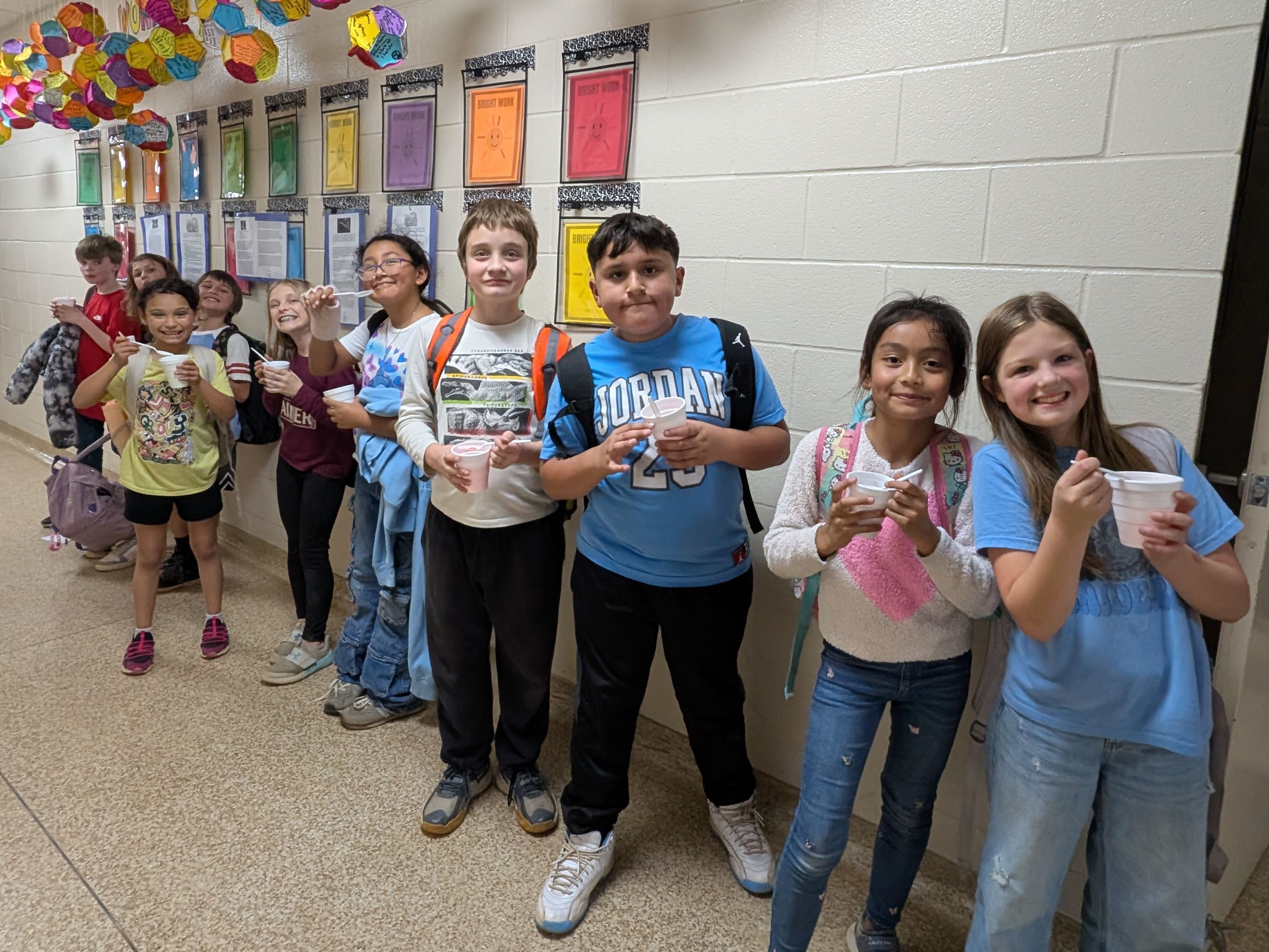 A group of young students standing in a colorful, decorated school hallway, surrounded by vibrant paper lanterns or decorations hanging from the ceiling.