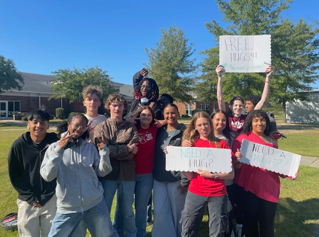 A group of people, mostly young adults, are standing together outdoors holding signs with messages related to a social or political cause.